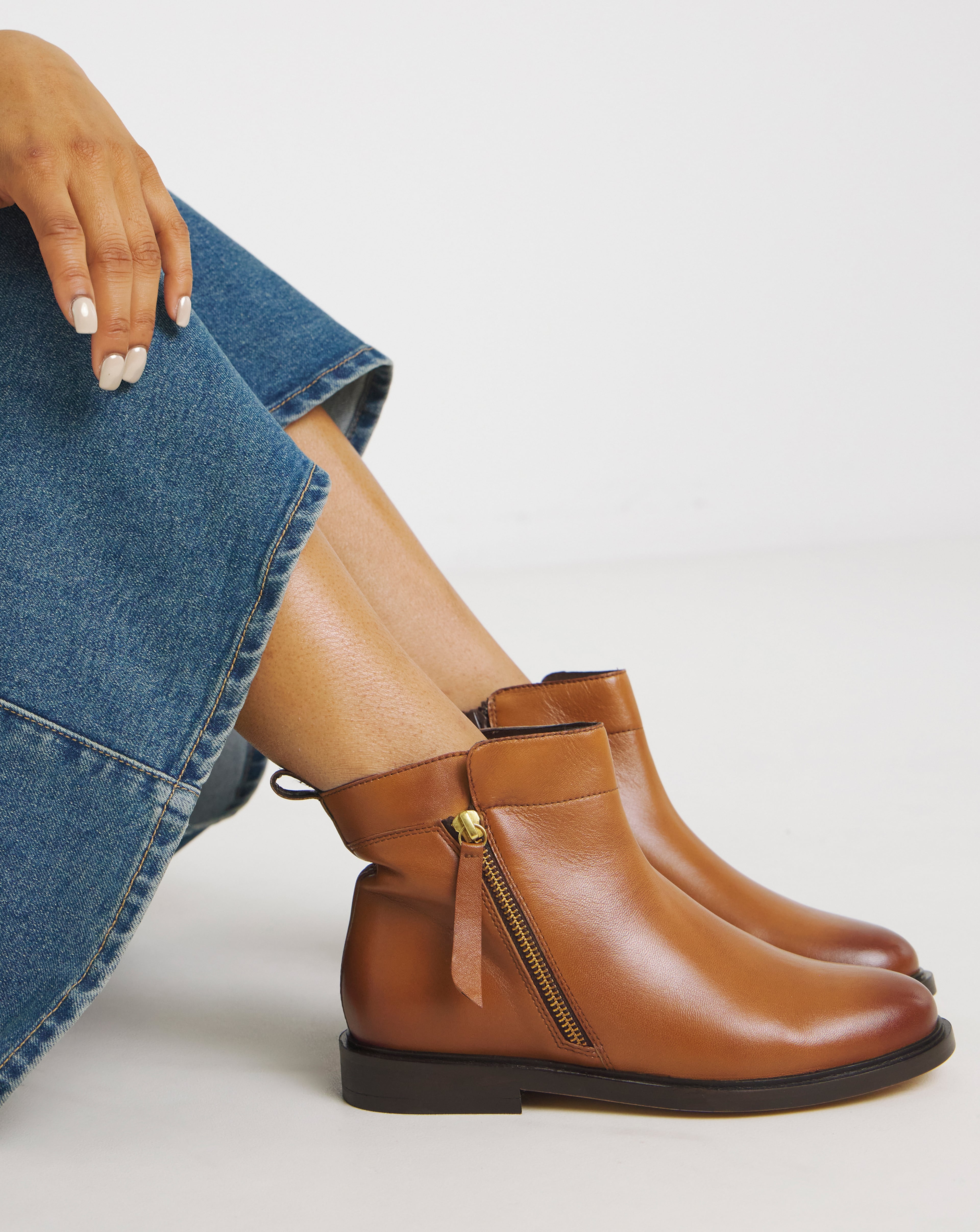 A person wearing blue jeans and brown leather ankle boots with a side zip.