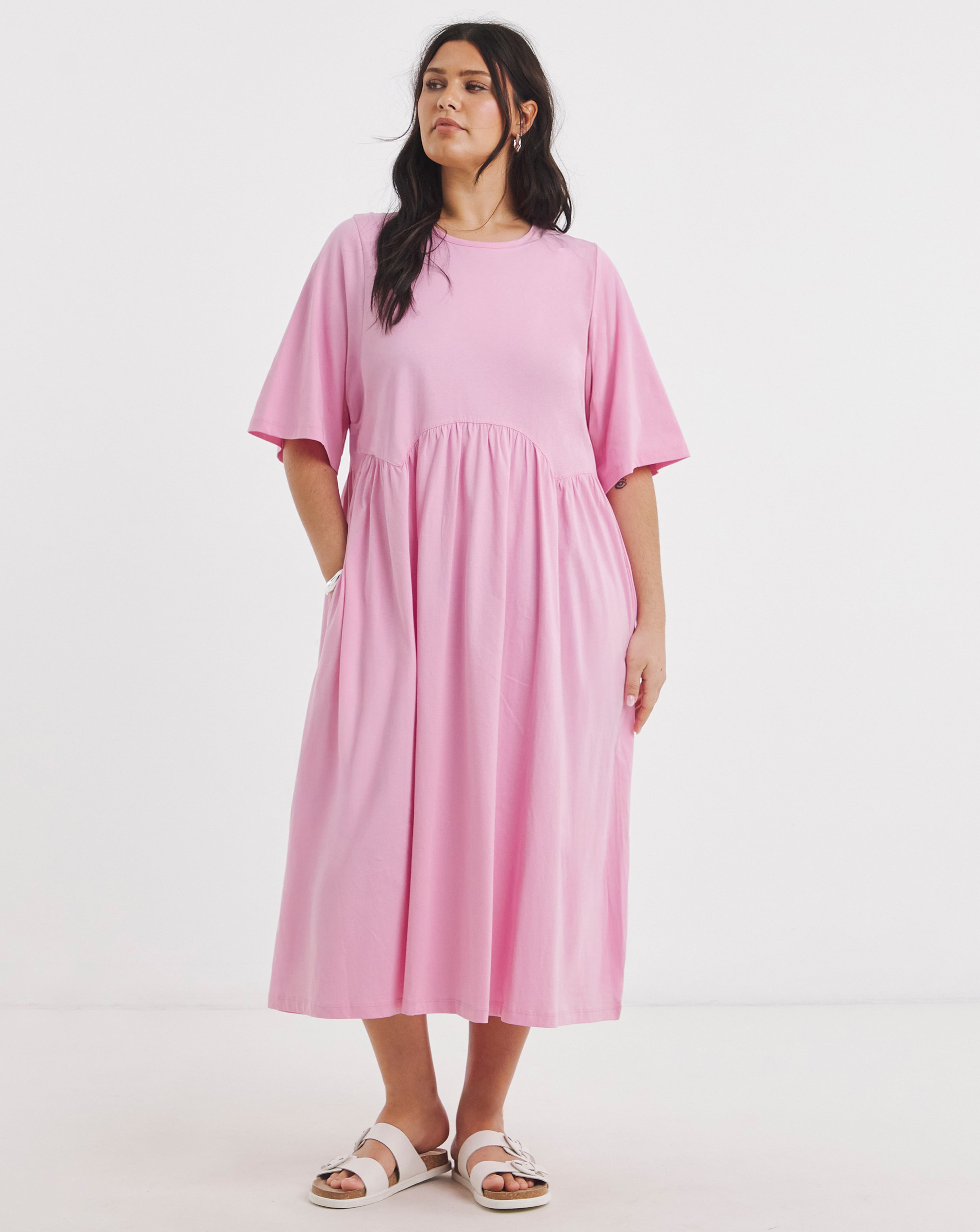 Person wearing a loose pink mid-length dress with short sleeves and white sandals.