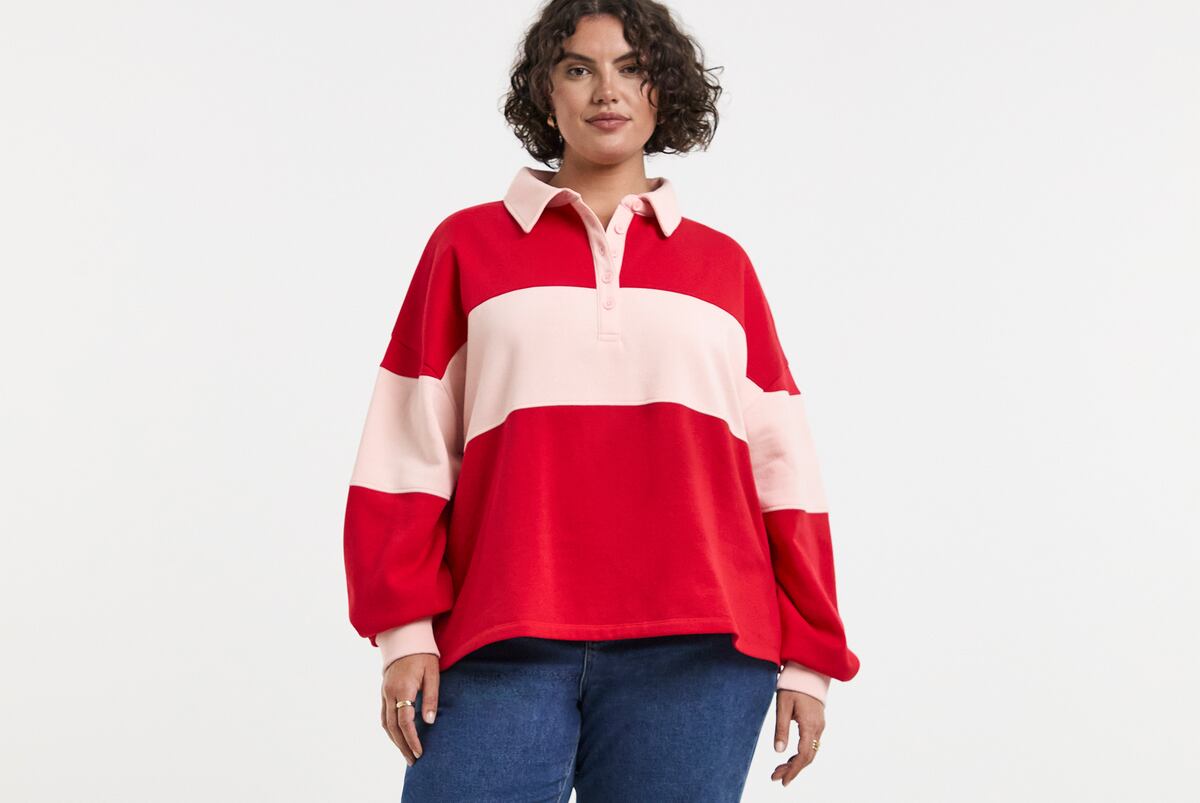 Person wearing a Simply Be red and pink polo sweatshirt with blue jeans.