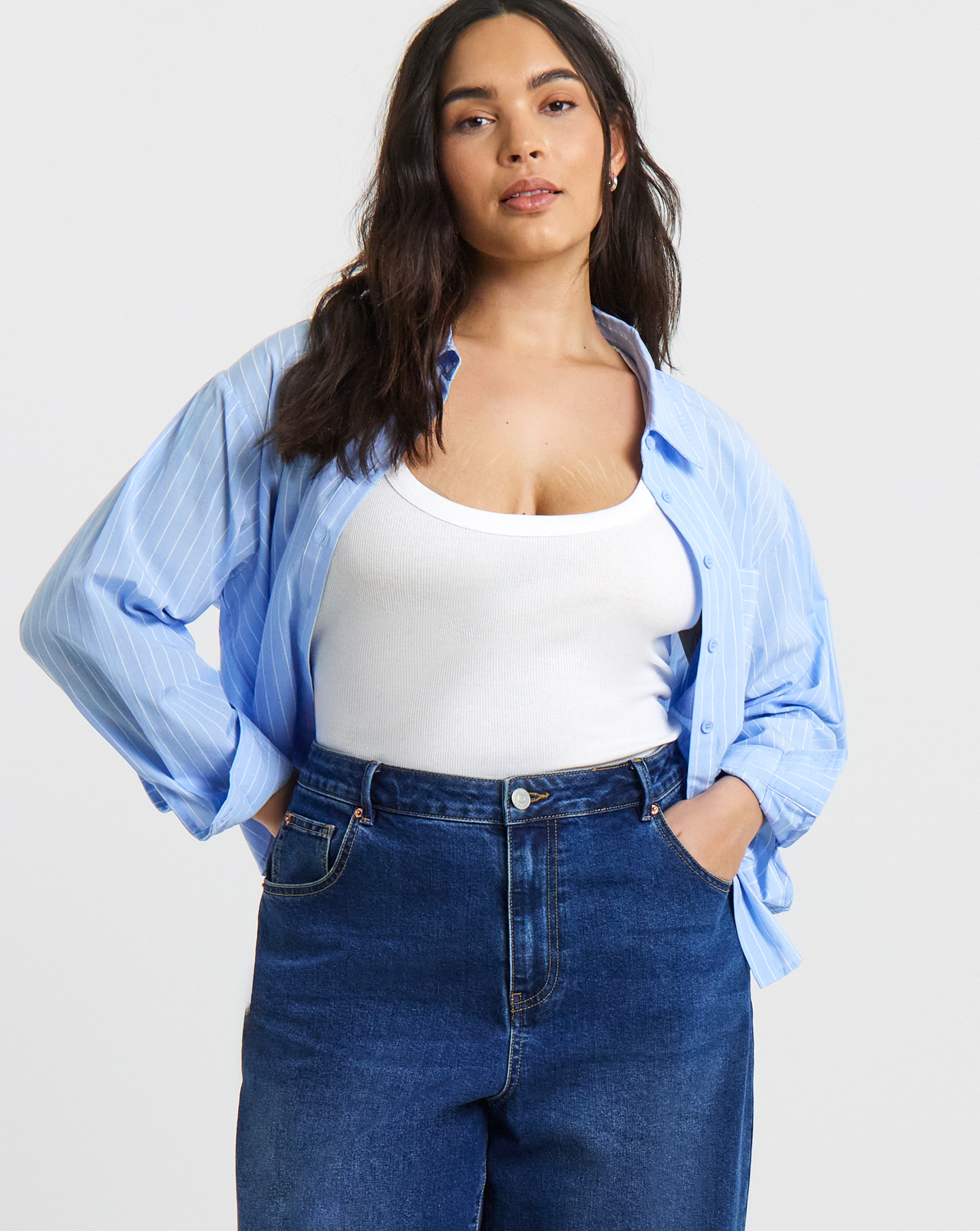 Person wearing a white vest top, light blue striped shirt and dark blue high-waisted jeans.