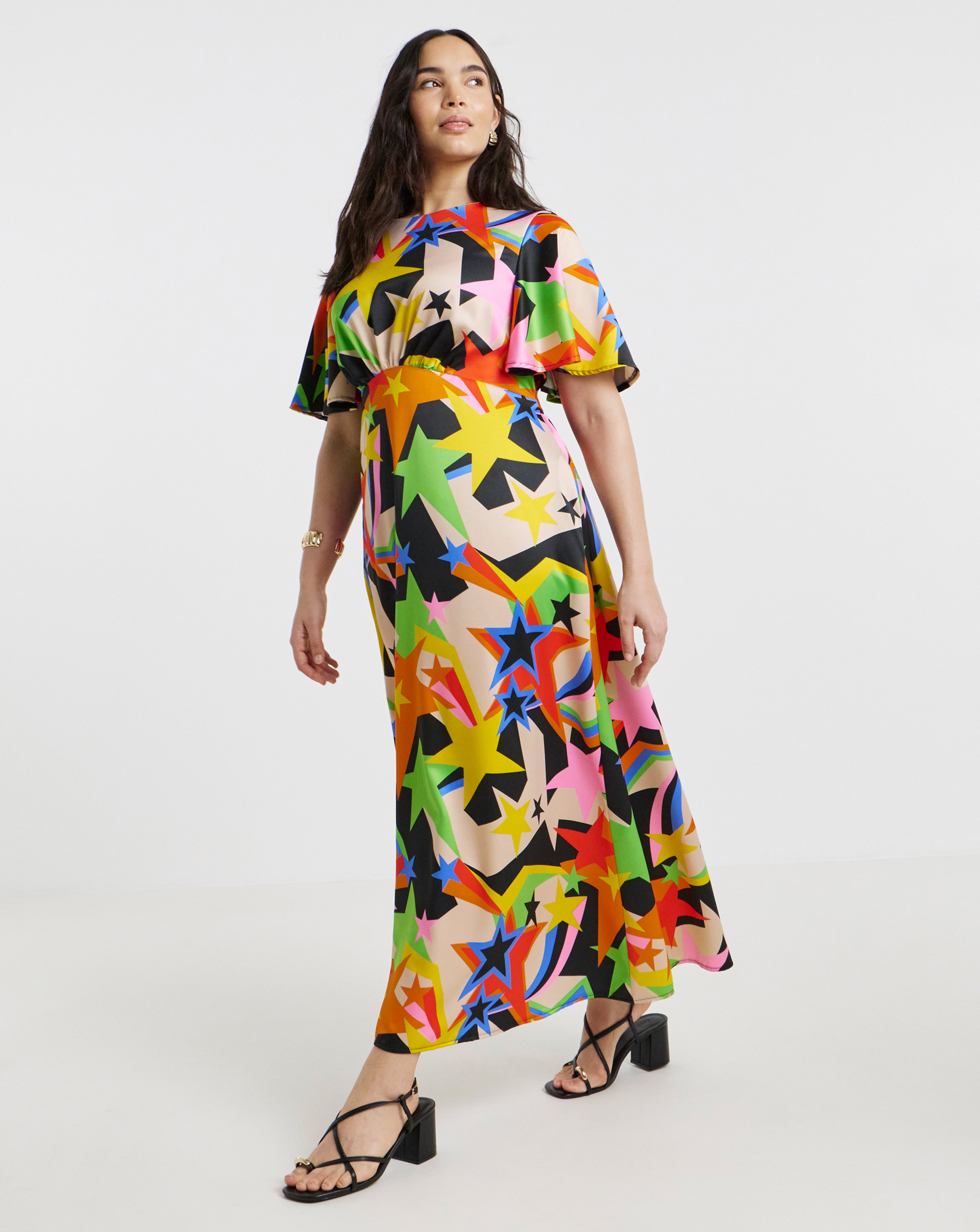 Person wearing a colourful star-print midi dress with flutter sleeves, paired with black heeled sandals.