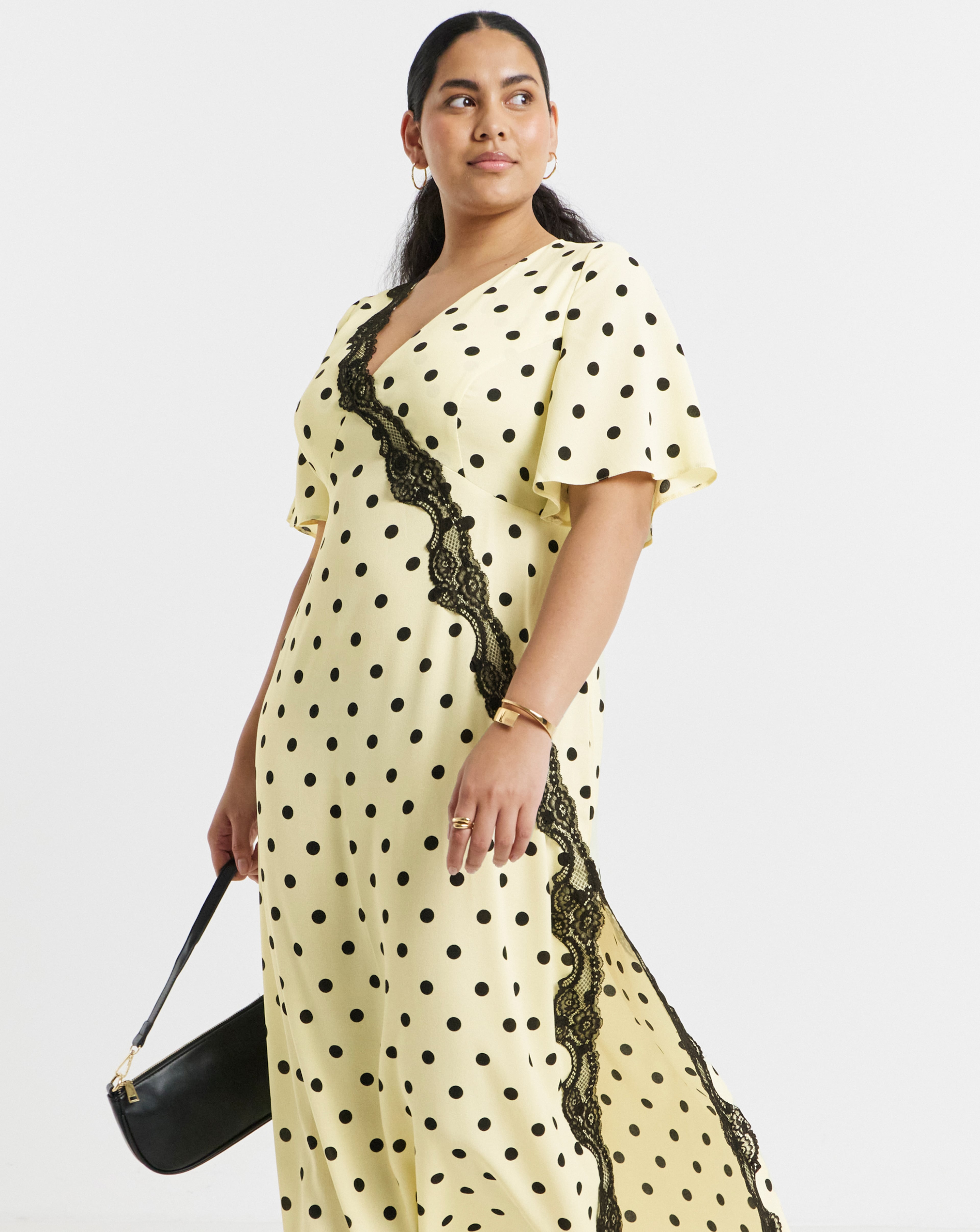 Person modelling a cream Simply Be polka-dot midi dress with black lace trim, styled with a black shoulder bag.