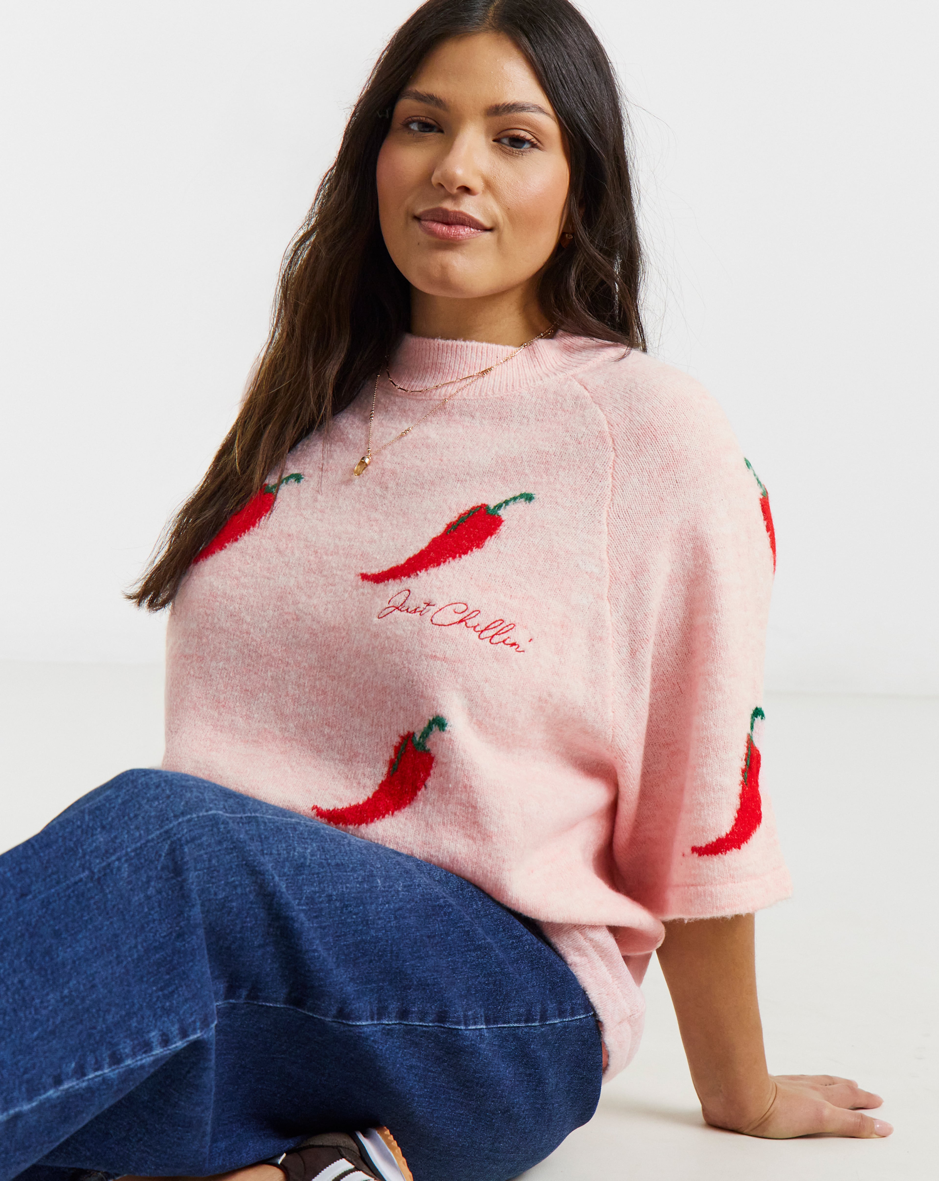 A person sitting down wearing a pink knit sweater with red chilli peppers and the slogan "Just Chillin'".