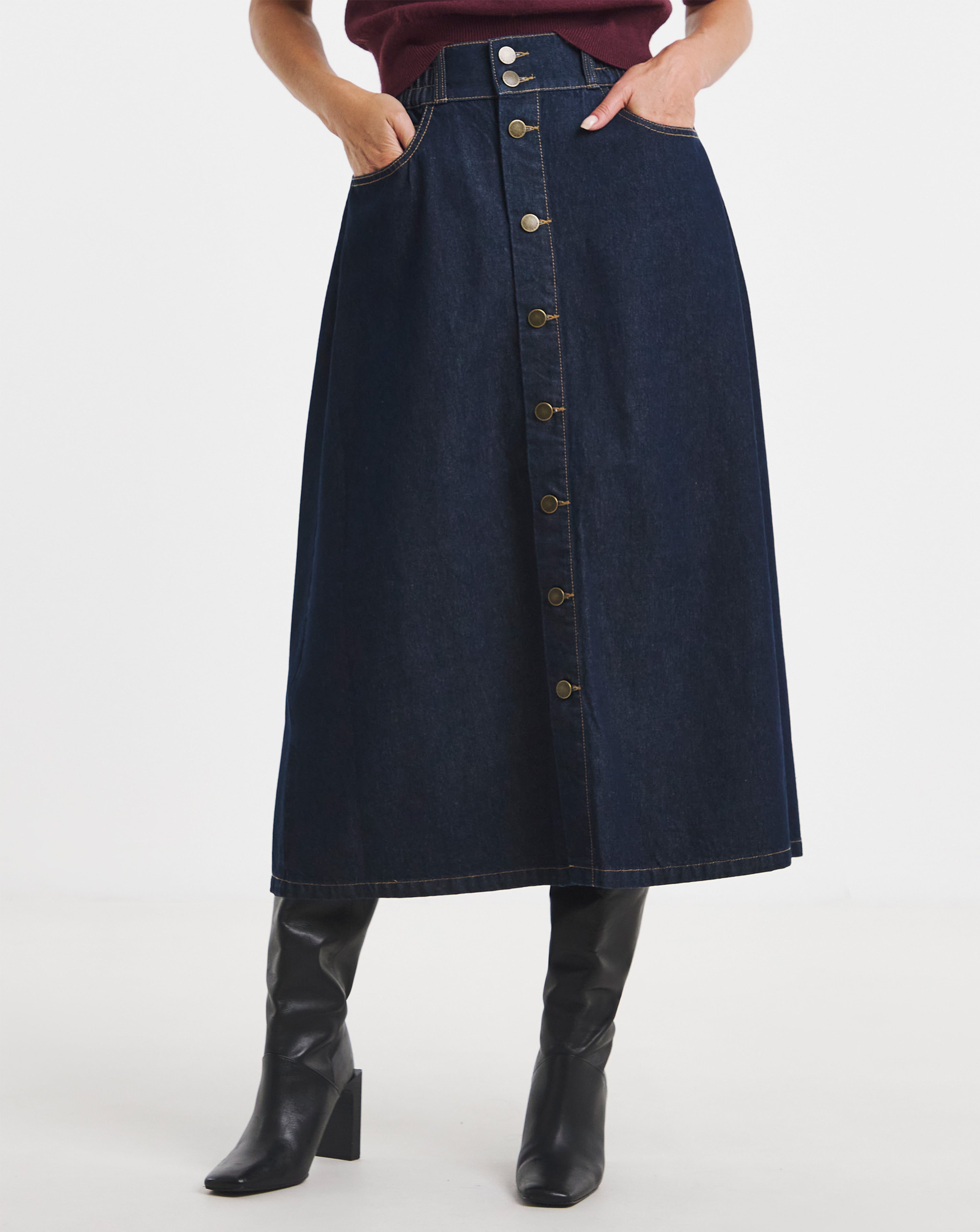Dark-wash denim midi skirt with front button fastening, styled with knee-high black boots.