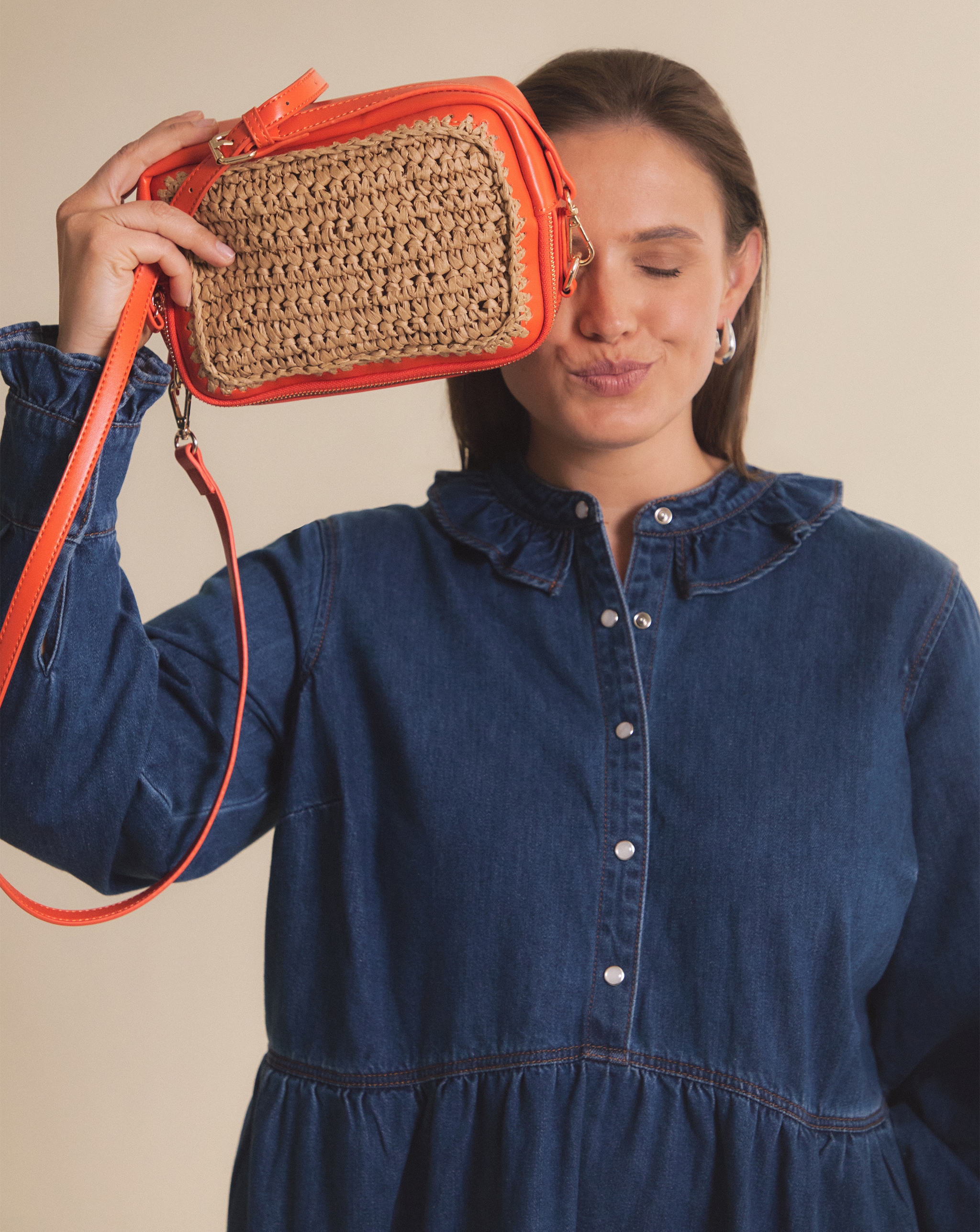 Person in denim dress holding a small woven handbag with orange trim