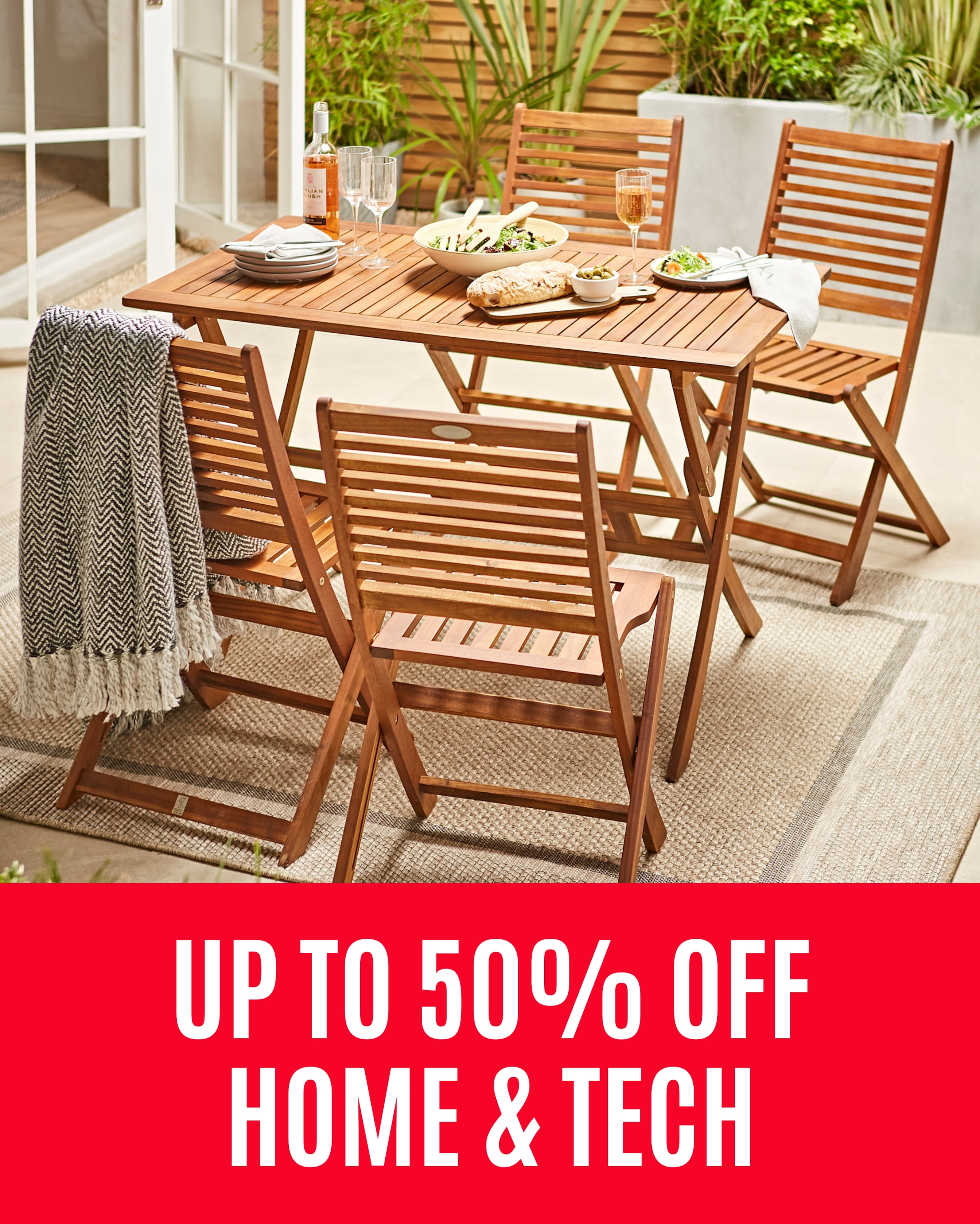 Wooden garden table and chairs set with food and wine, beside an open patio door and plants, with a sale message overlaid.