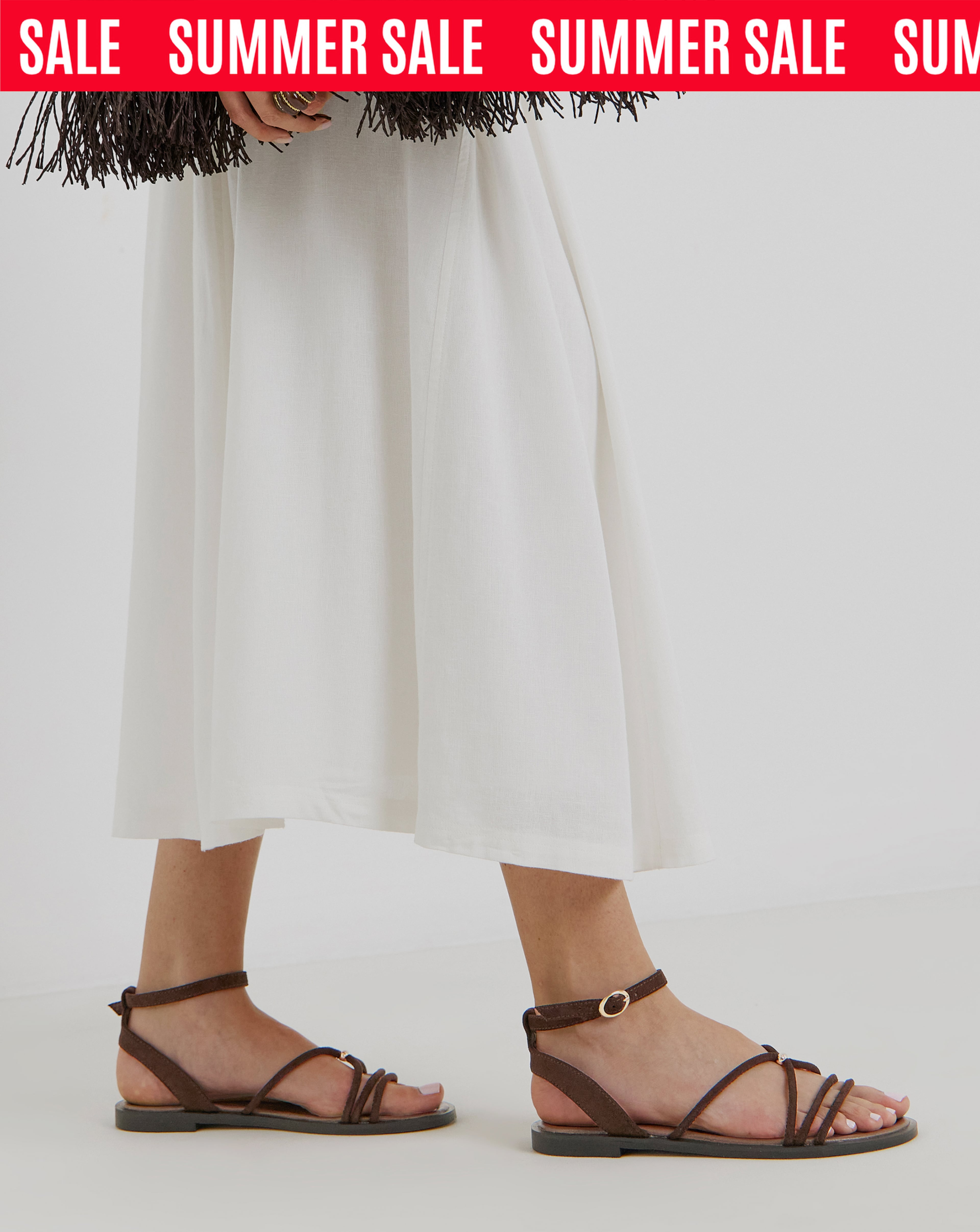Summer sale banner showing brown strappy flat sandals worn with a flowing white midi skirt.