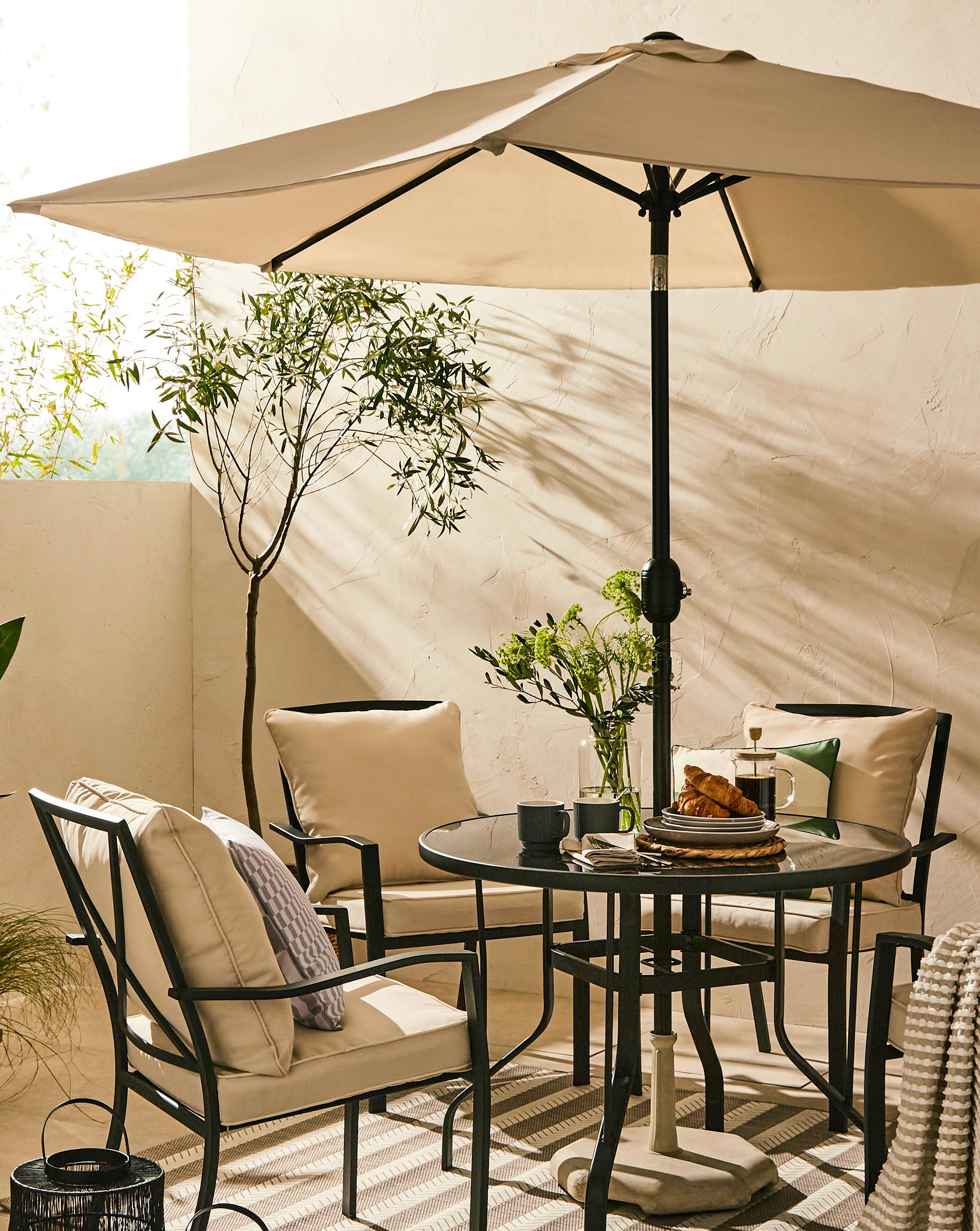 Outdoor patio with a round glass table, four garden chairs, and a beige umbrella.