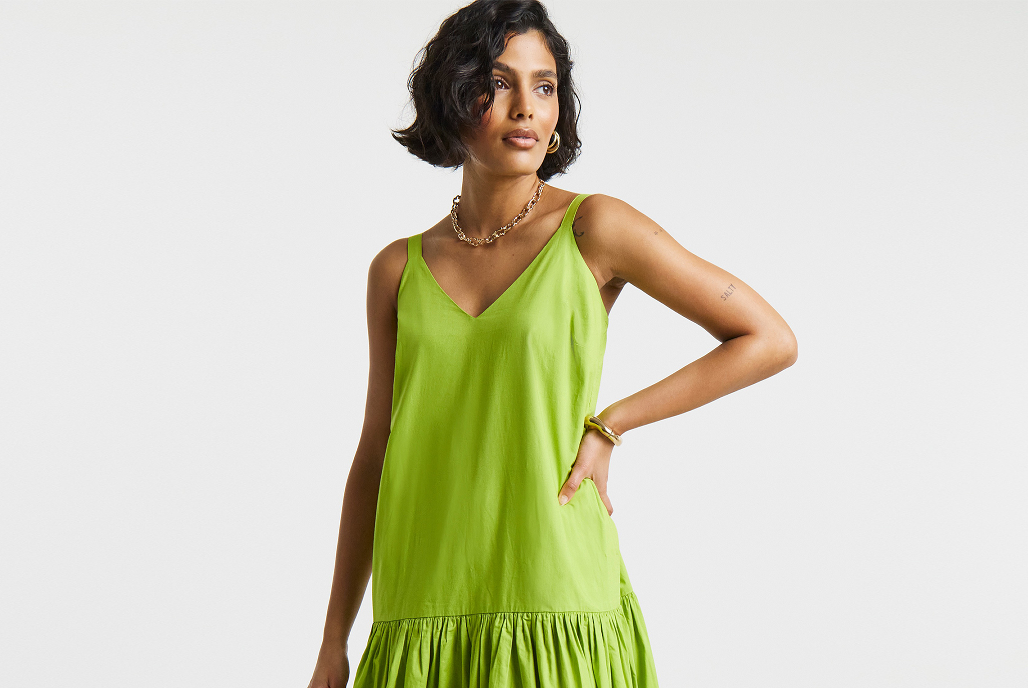 Person wearing a chartreuse-coloured sleeveless midi dress, styled with gold jewellery,