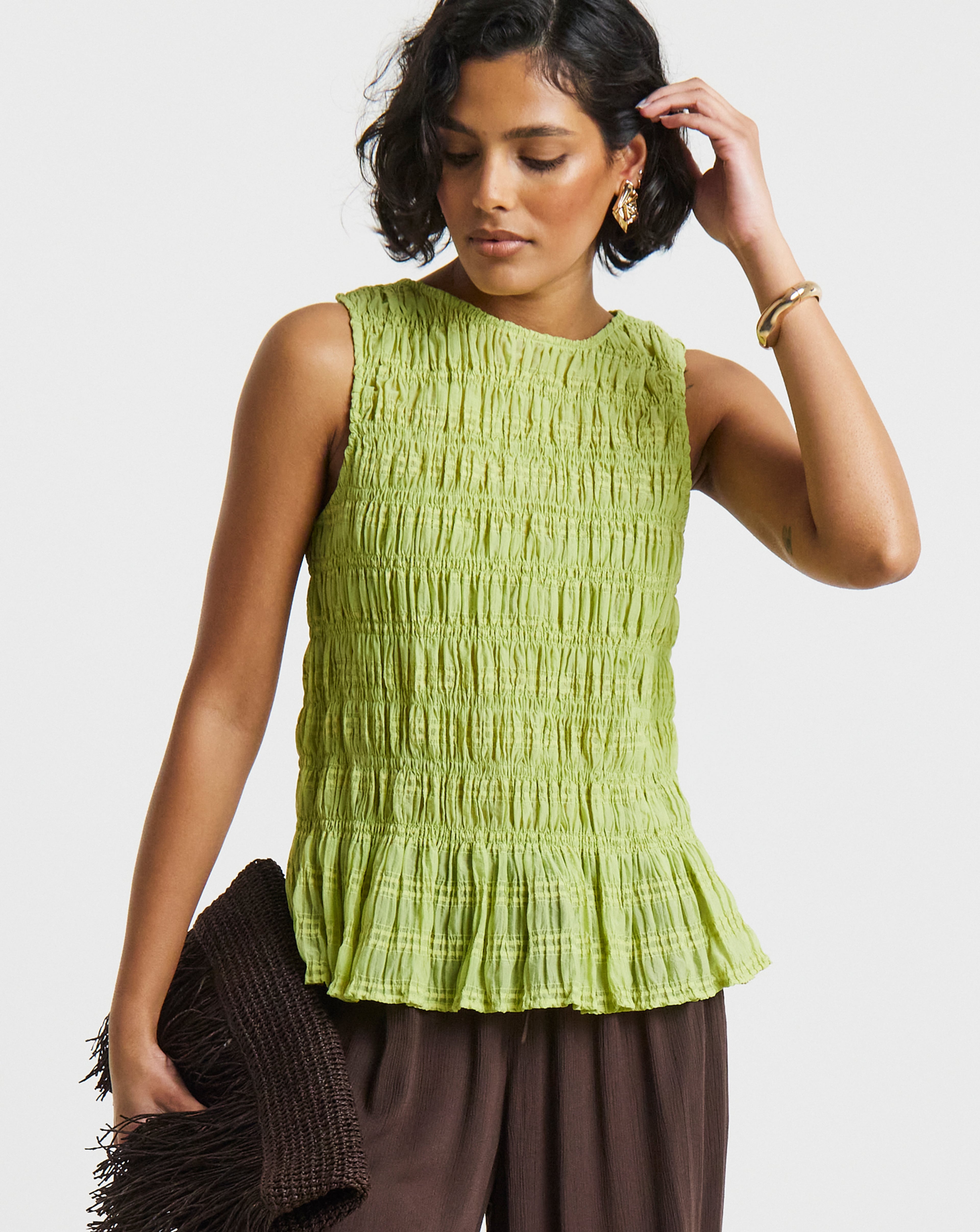 Close-up of a person wearing a textured green sleeveless top with gold jewellery.