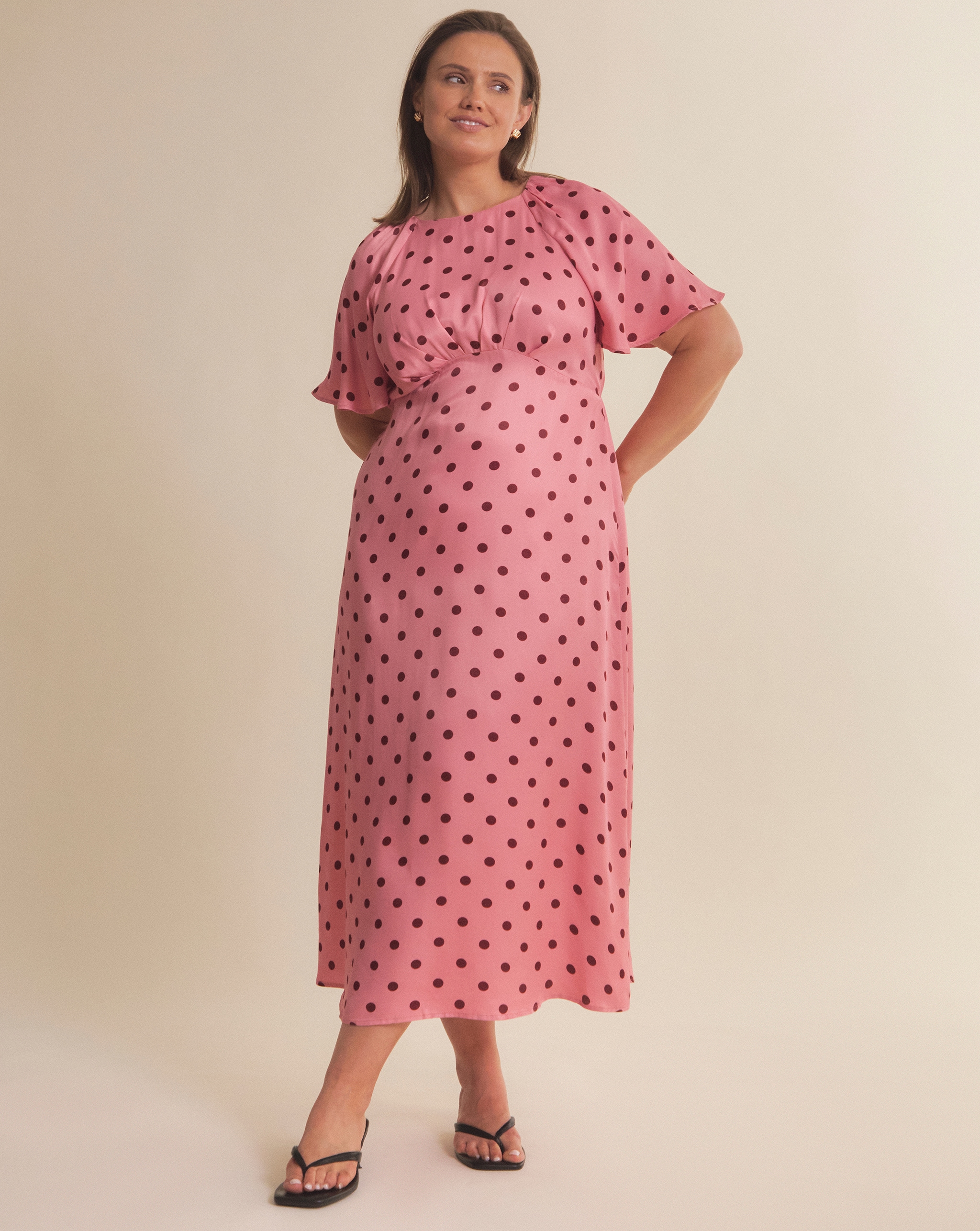 Person in a pink dress with black polka dots, standing with hands on hips