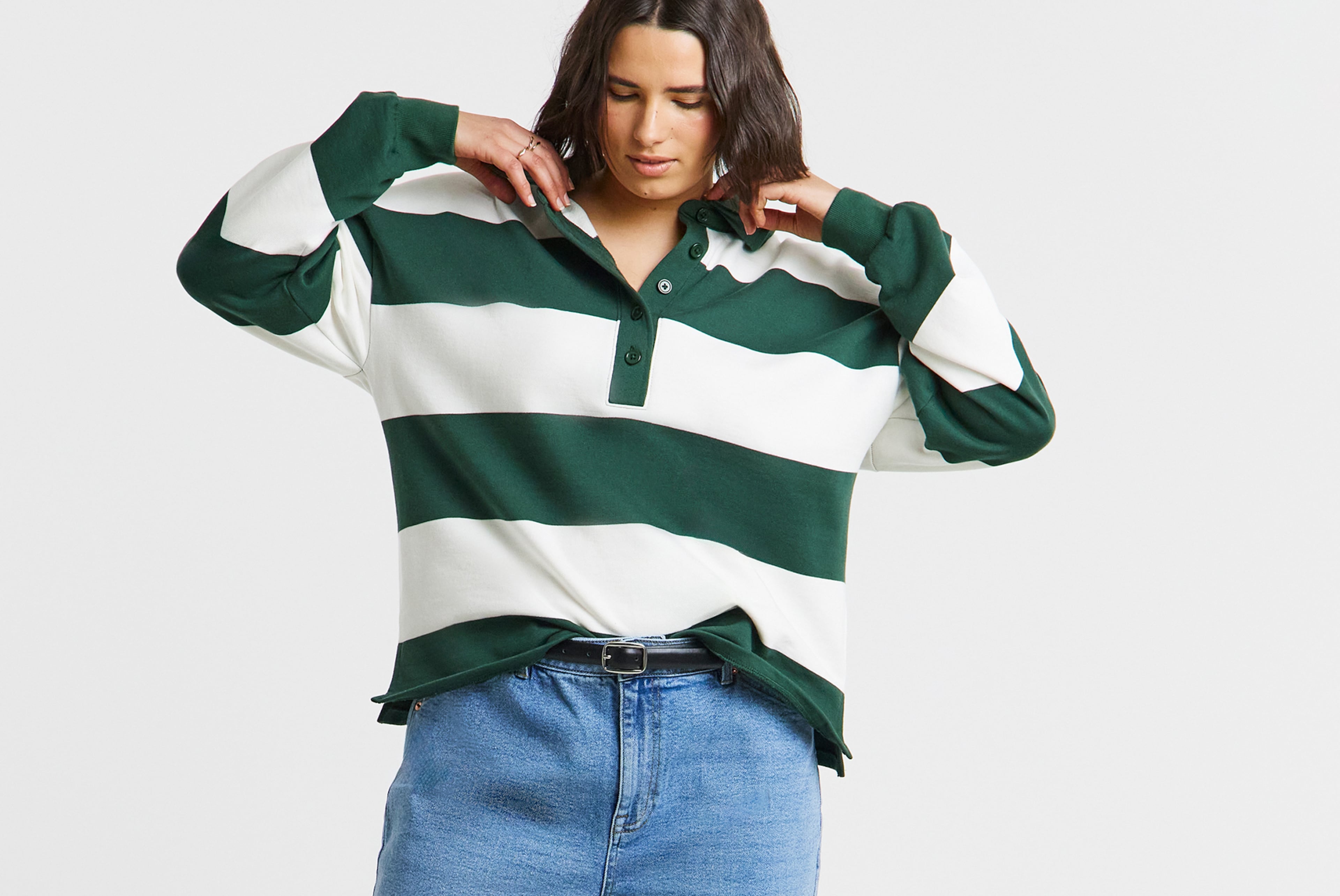 Person wearing a green‑and‑white striped long‑sleeve polo shirt, tucked into blue jeans.