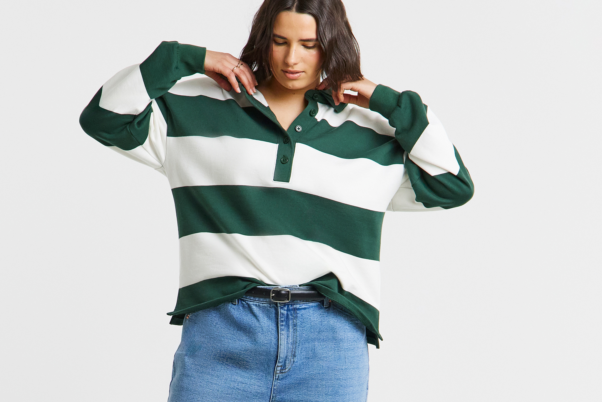 Person wearing a green‑and‑white striped long‑sleeve polo shirt, tucked into blue jeans.