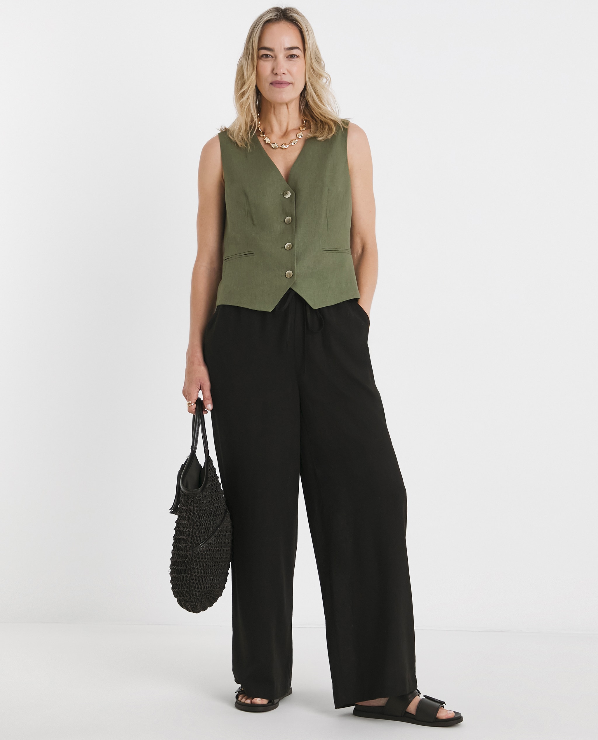 Model is wearing a khaki button waistcoat with a pair of black linen mix wide leg trousers.