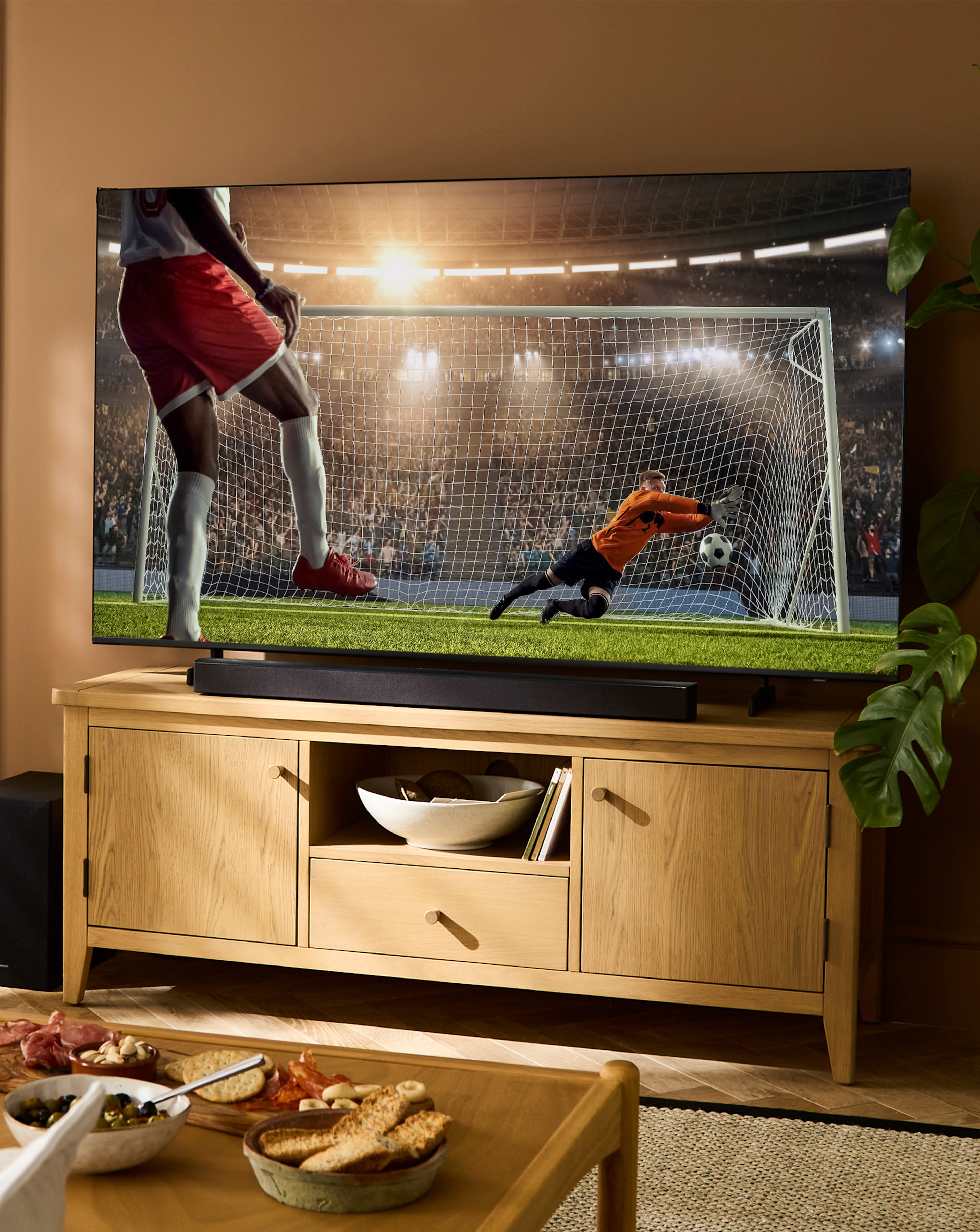 Living room scene featuring a TV showing a football match, with snacks on a coffee table in the foreground.