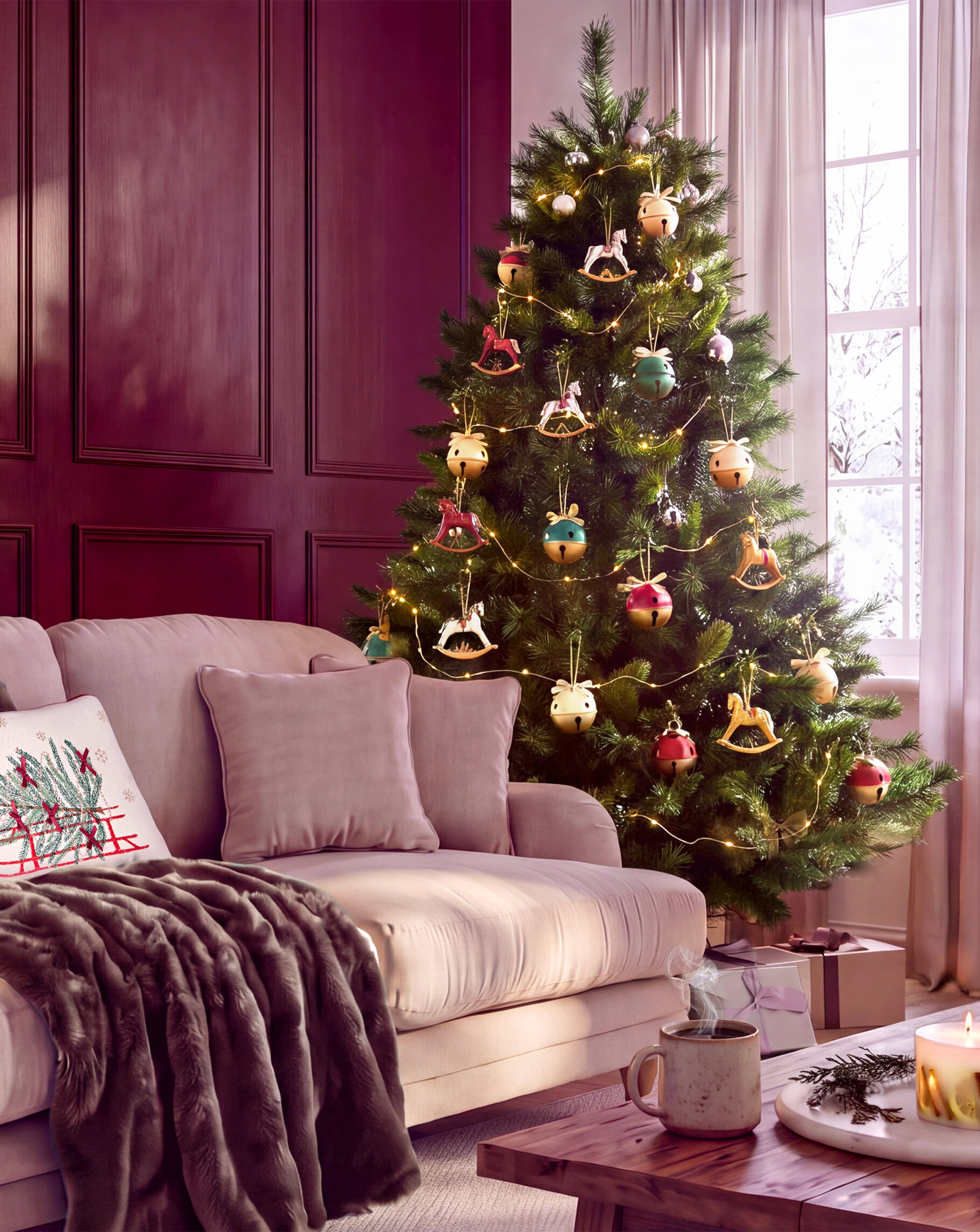 Festive living room with a decorated Christmas tree, wrapped gifts, a pink sofa, and a coffee table with a candle and steaming mug.