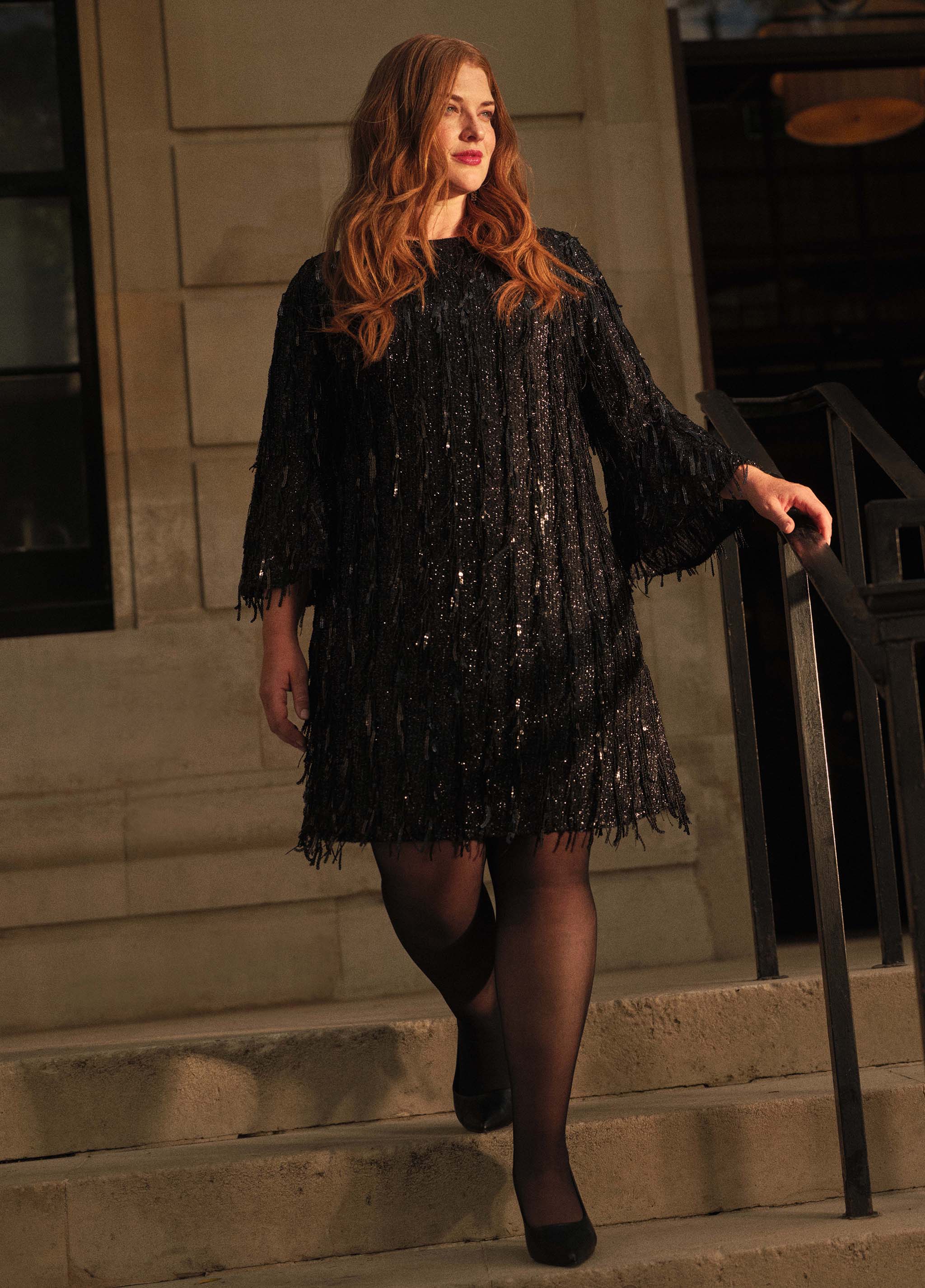 A lady walking down some steps wearing a black sequin dress.