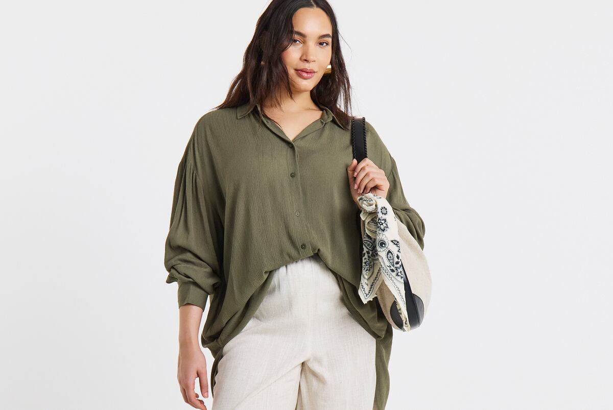 Person wearing an olive-green button-up shirt with loose sleeves, holding a black shoulder bag.