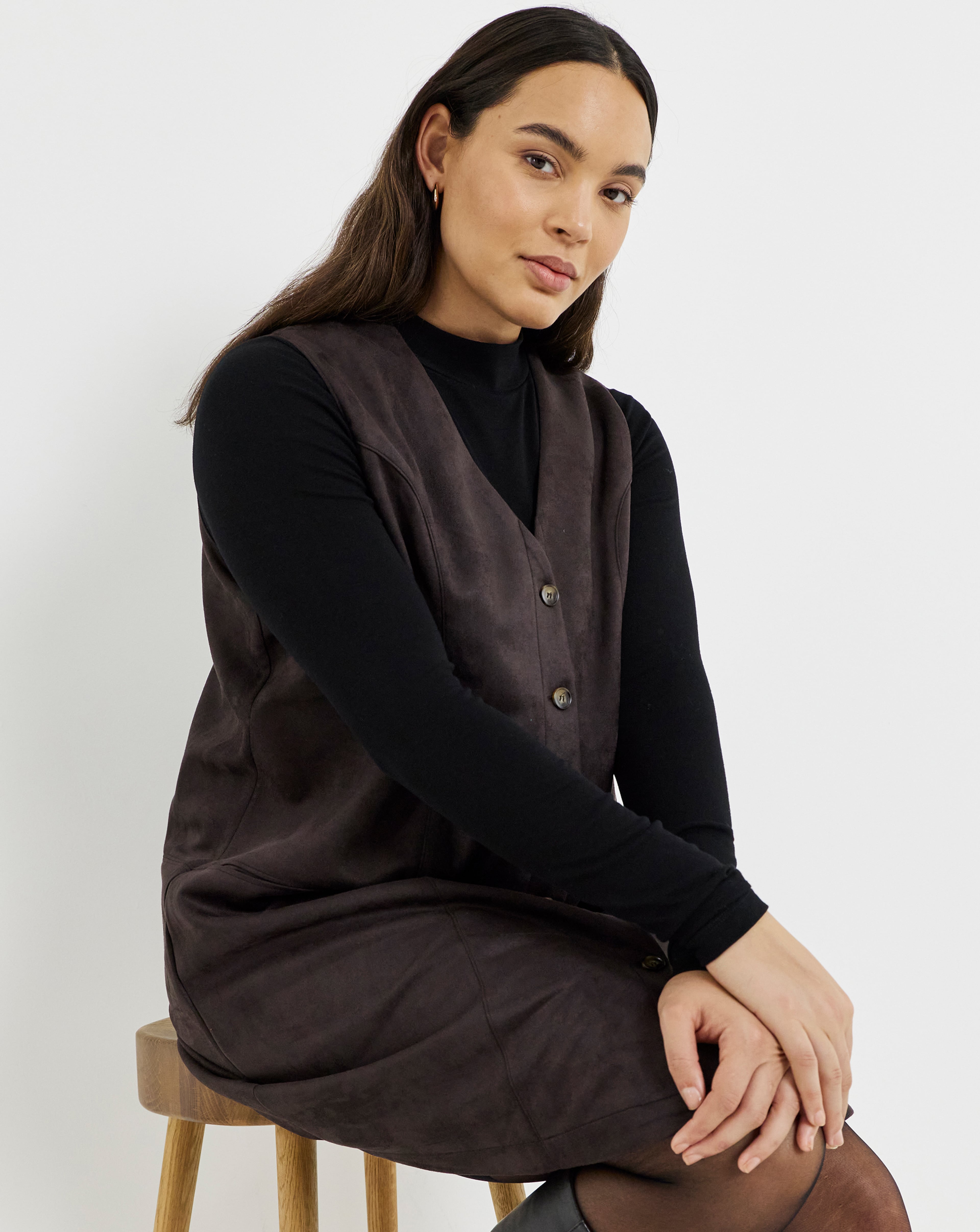 A person wearing a chocolate-coloured suedette sleeveless dress over a black long-sleeve top.