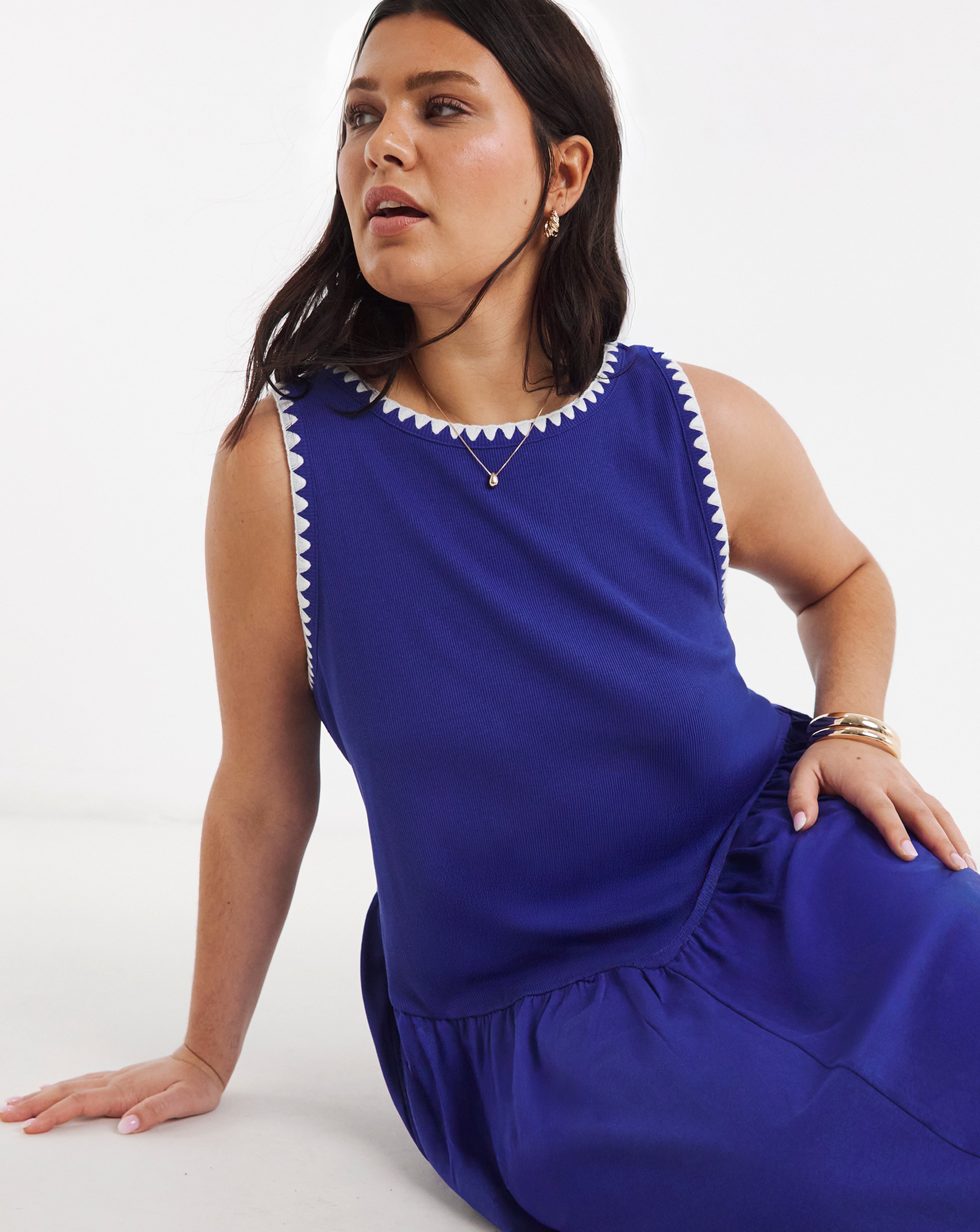 Close-up of a person seated, wearing a sleeveless blue dress with white trim details.