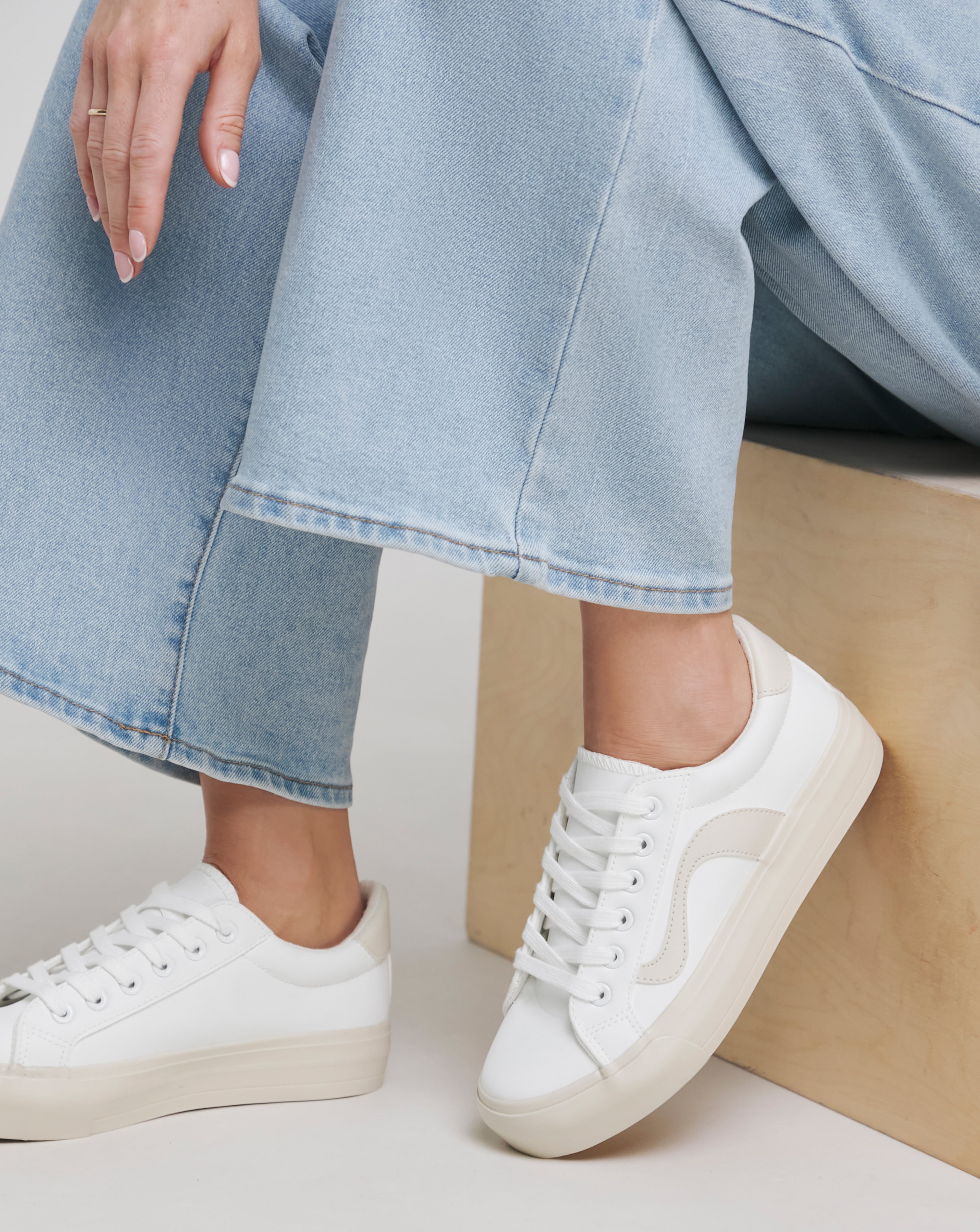 Close-up of cropped light blue denim jeans, paired with white platform trainers.