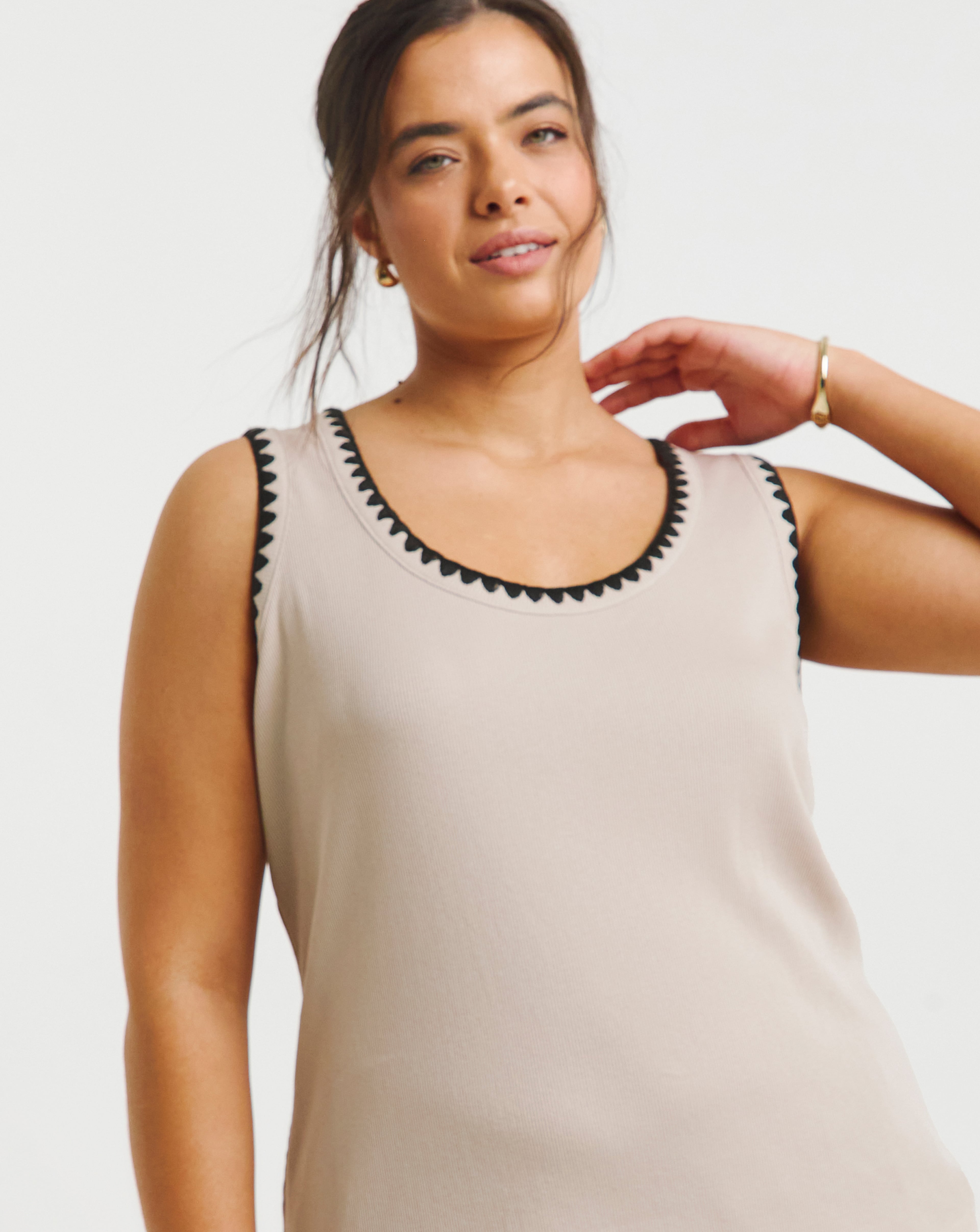 Close-up studio shot of a person wearing a sleeveless light beige top with contrasting dark trim.