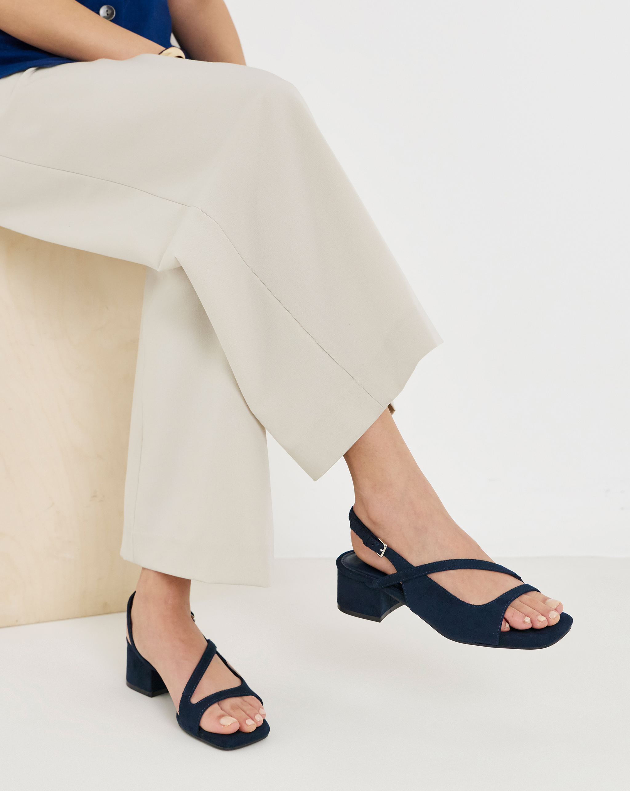 Close‑up of light cropped trousers with navy low‑heeled sandals.