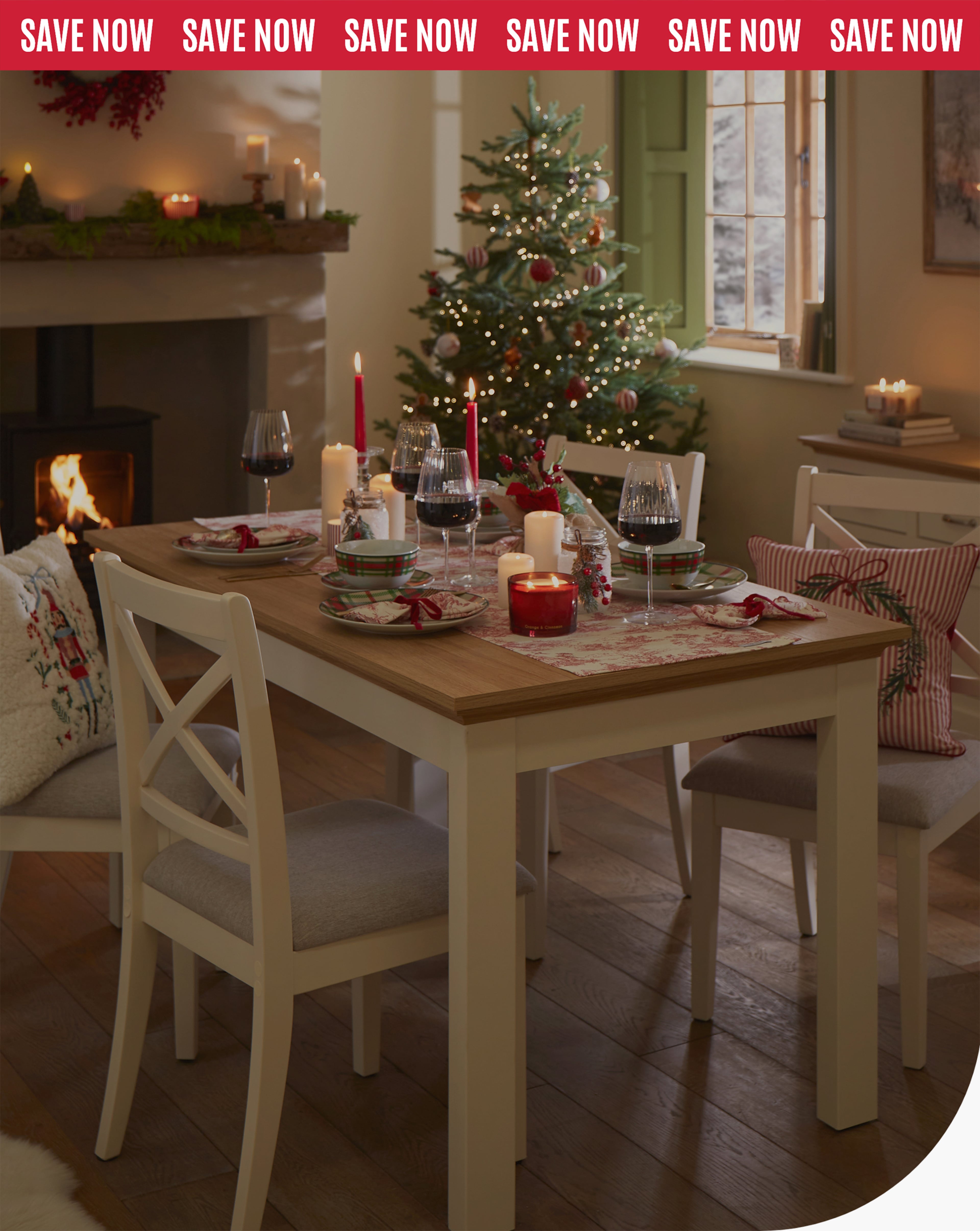 Dining table set for Christmas with candles, wine glasses, festive plates, and a decorated tree in the background.