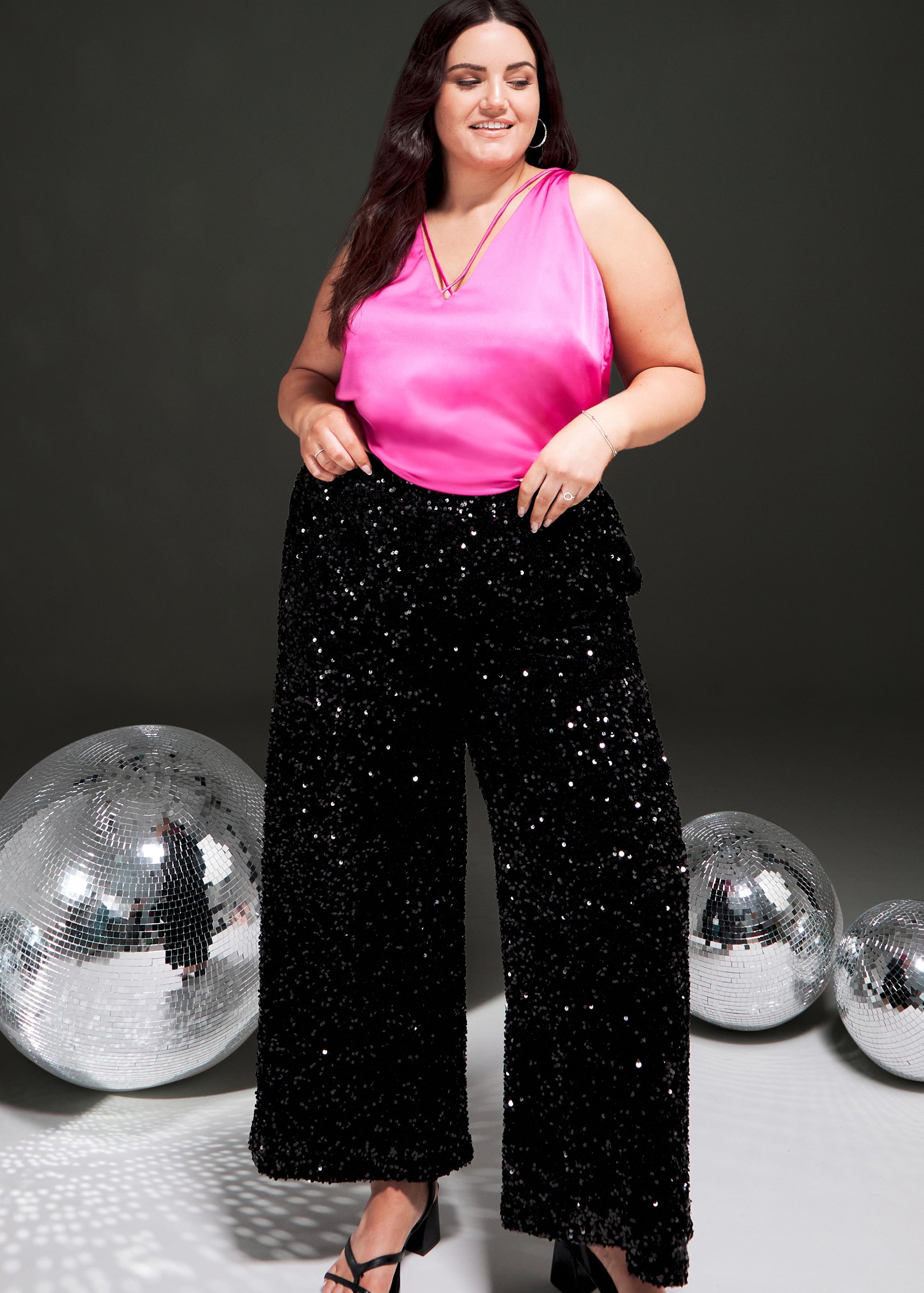 A woman stood wearing a sparkly pink vest top and sparkly black trousers