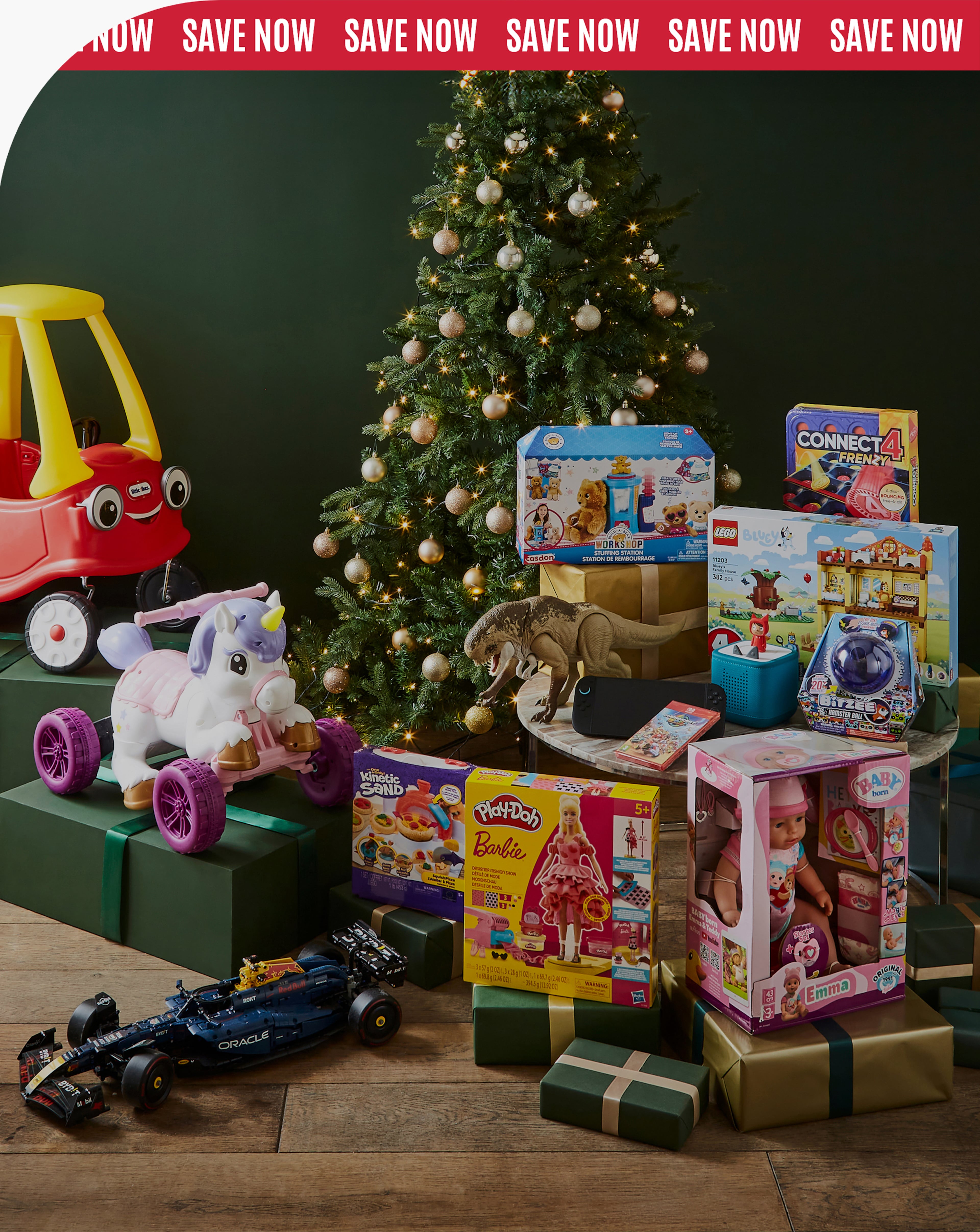 Assorted children’s toys and games stacked near a decorated Christmas tree with wrapped presents.