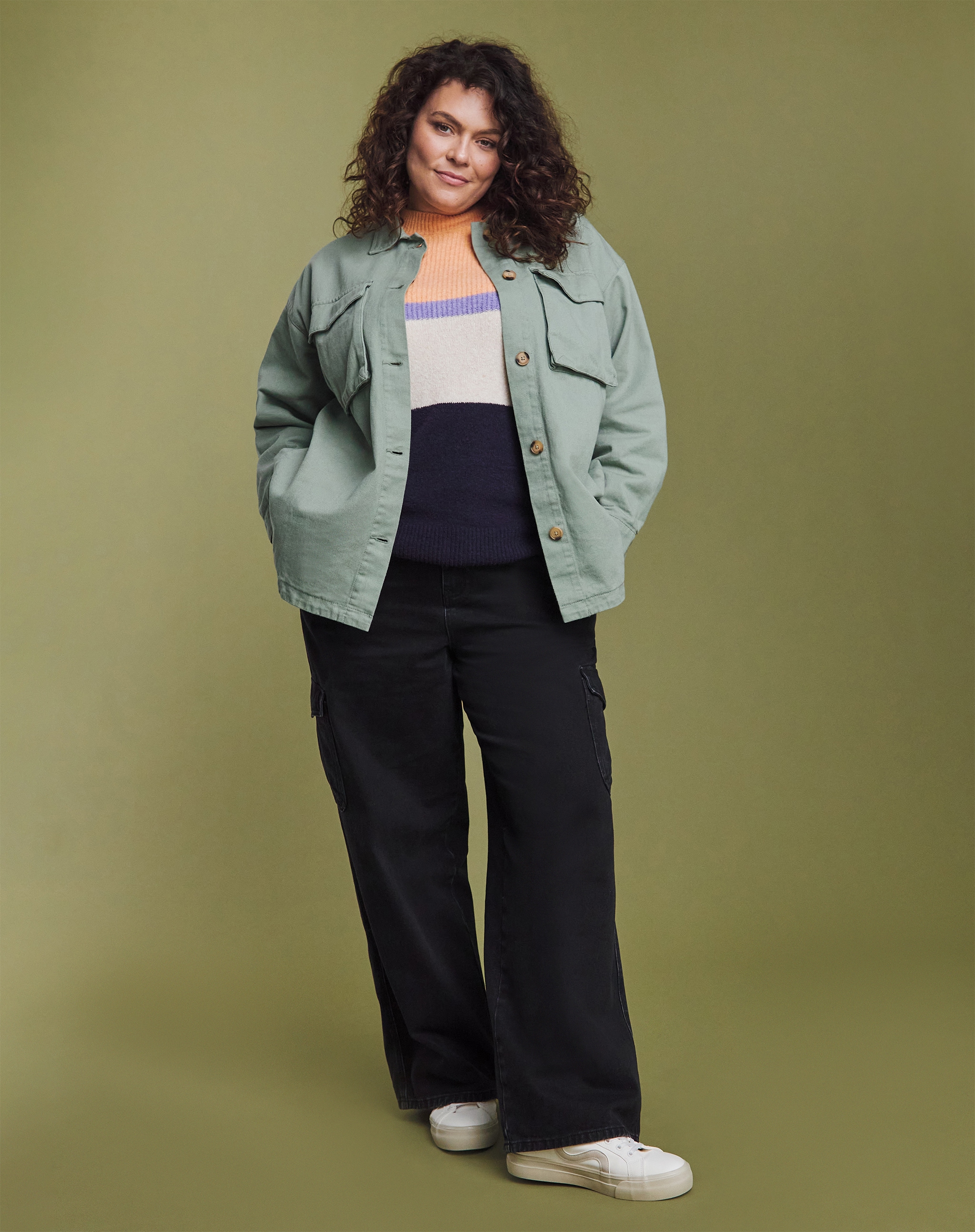 A woman stood wearing a mint green short jacket with flared black trousers