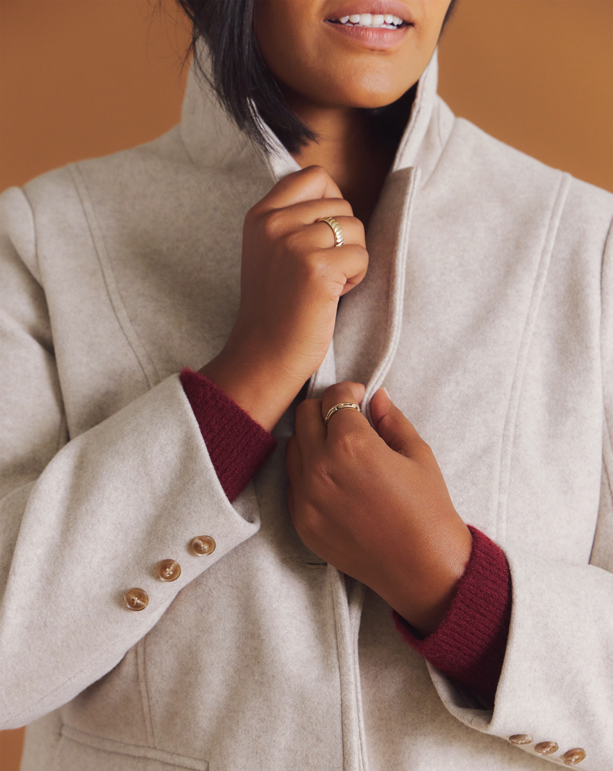 Person adjusting the collar of a light grey coat with maroon sleeves.