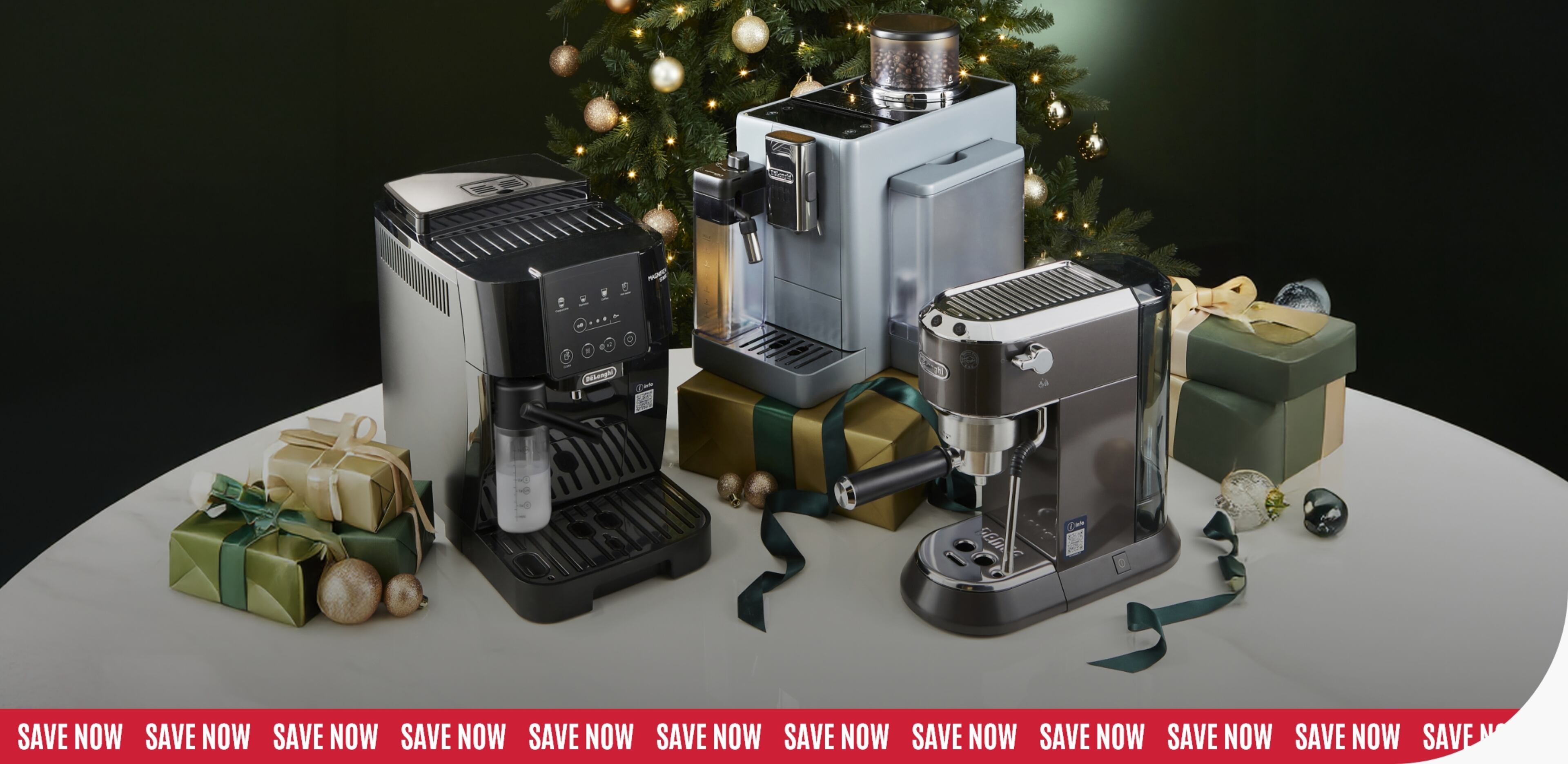 A festive display featuring three coffee machines on a round white table, surrounded by wrapped gift boxes.