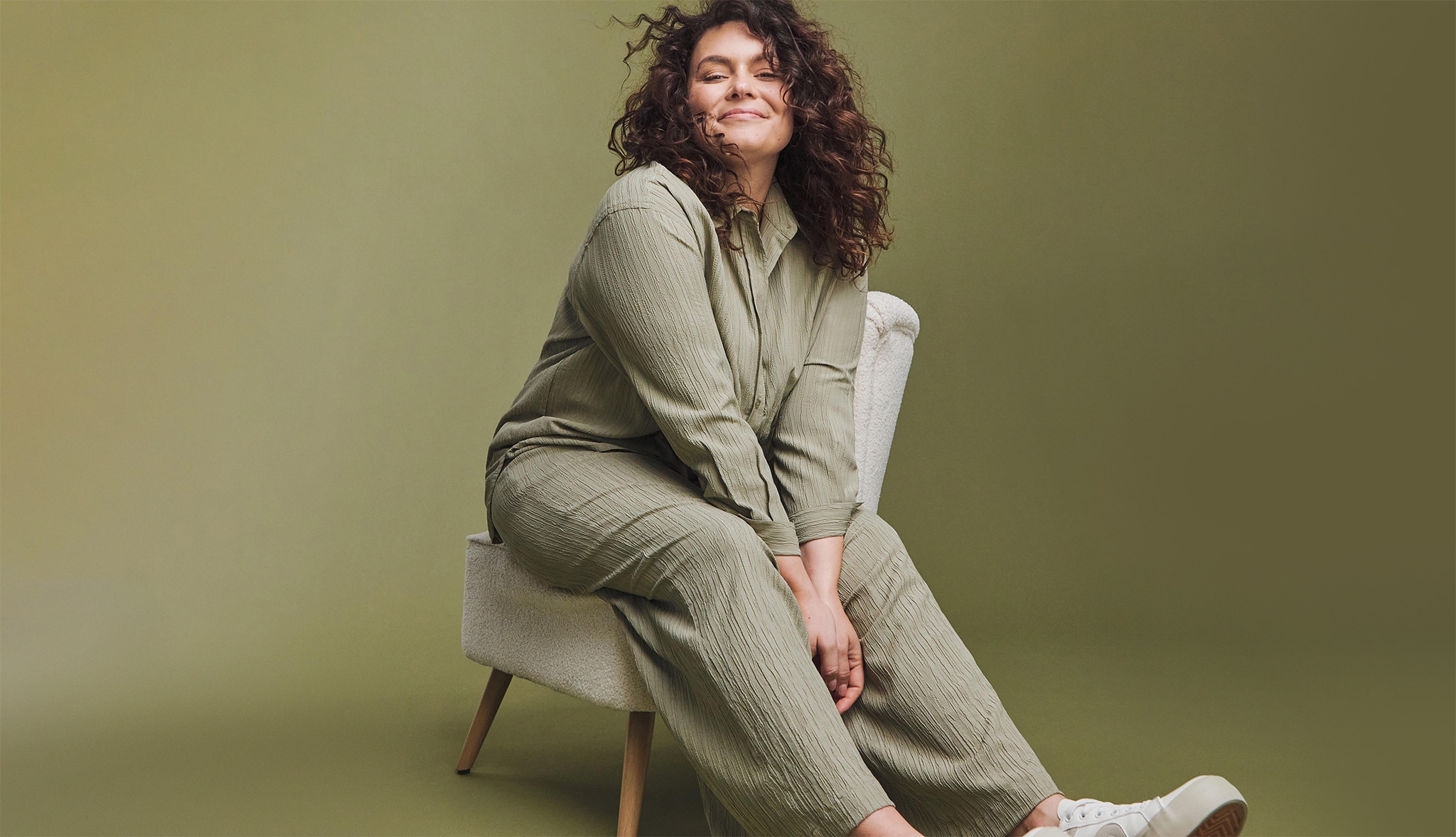 A woman sat on a chair wearing a green loose fit jumpsuit
