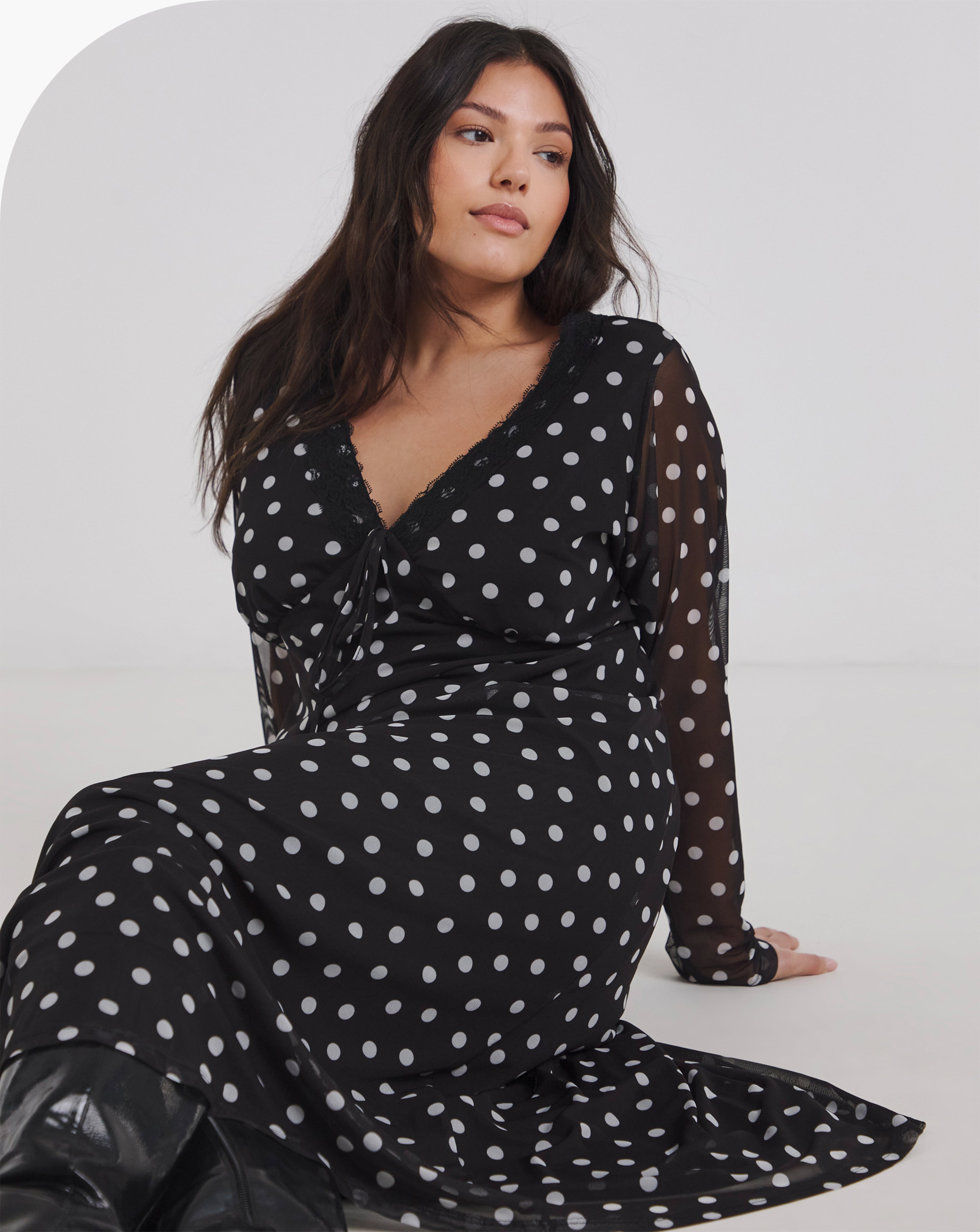 A model sat down, wearing a spot print midi dress. 