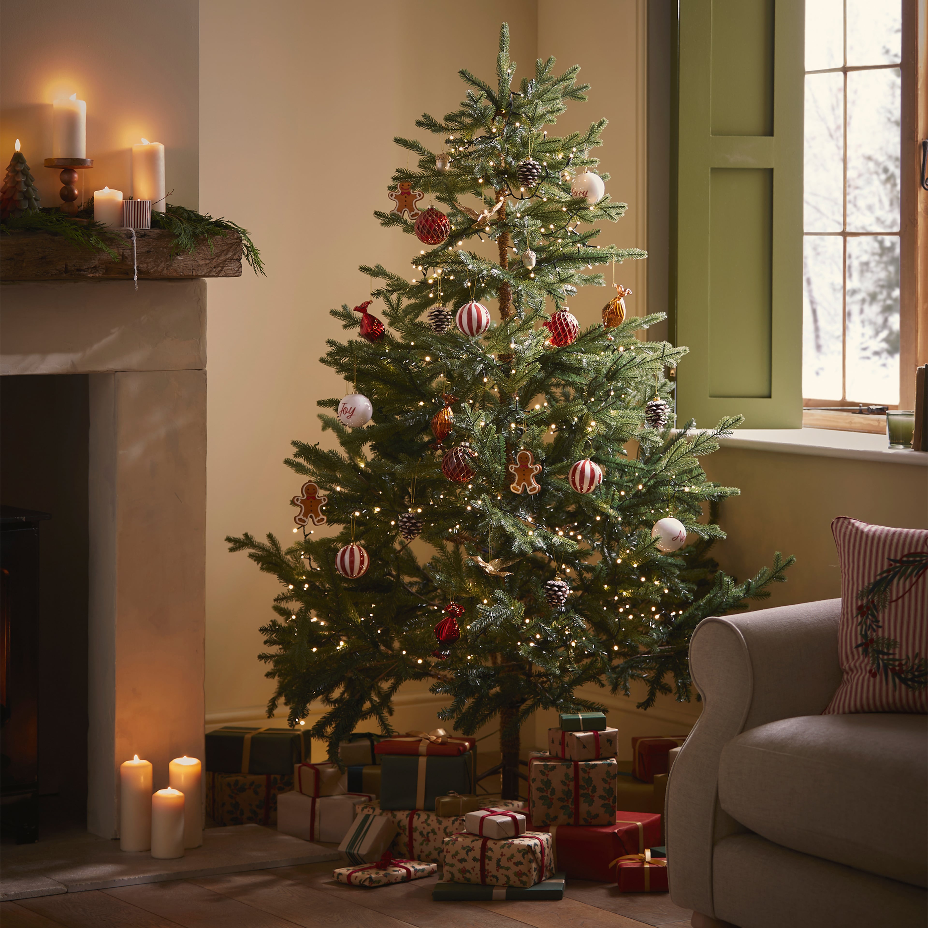 A living room with a decorated Christmas tree with presents underneath, next to a fireplace.