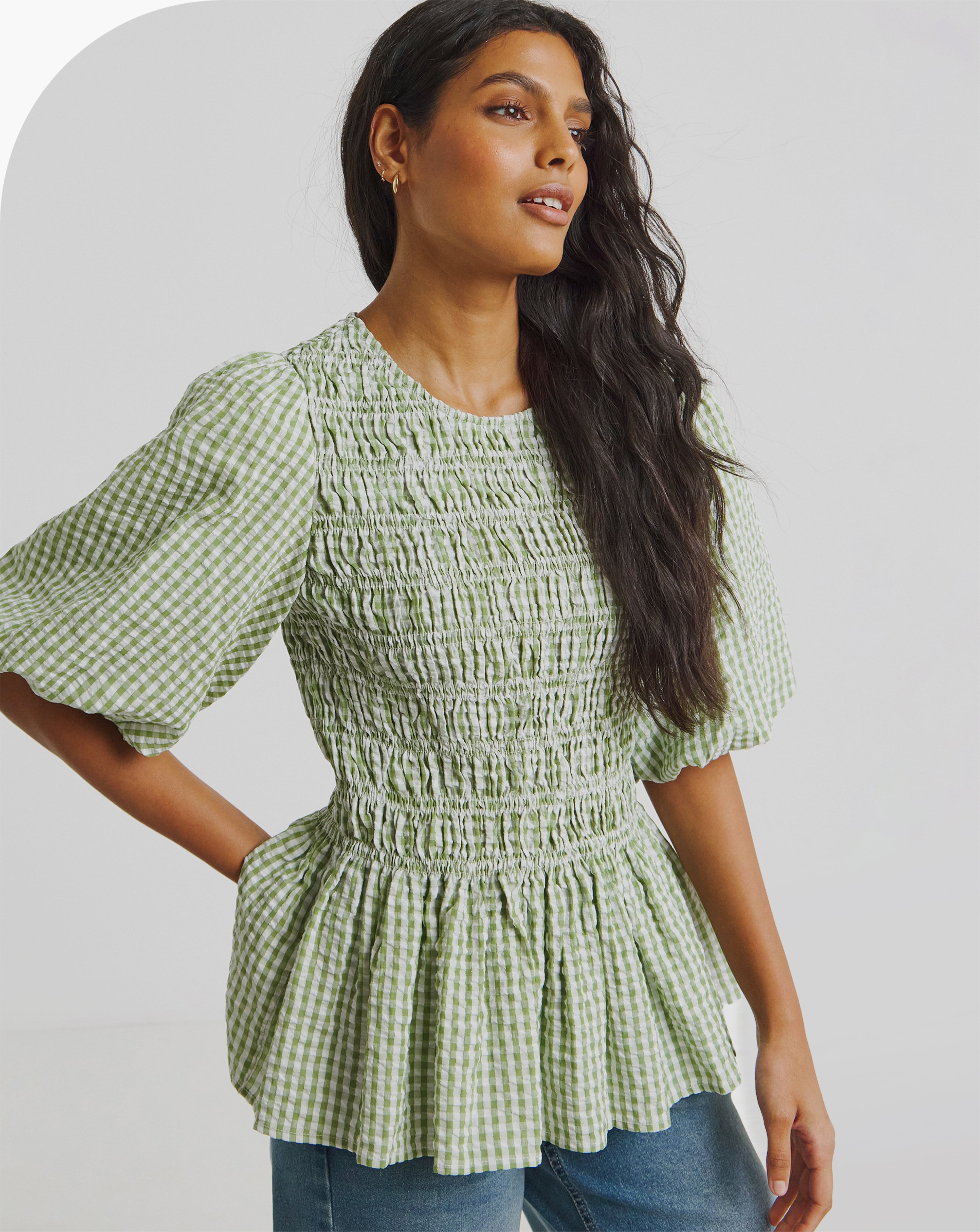 A woman wearing a Gingham Shirred Seersucker Blouse and blue jeans.