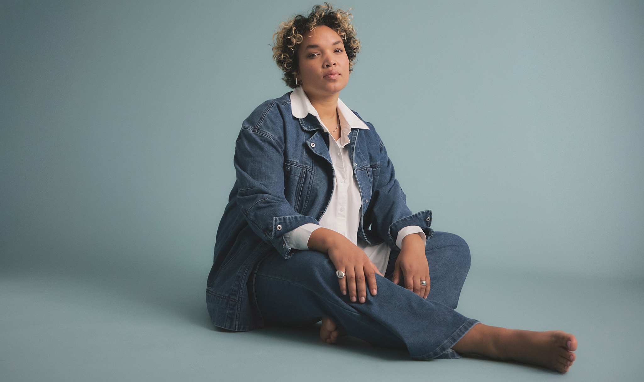 A woman sat on the floor wearing a denim jacket and jeans