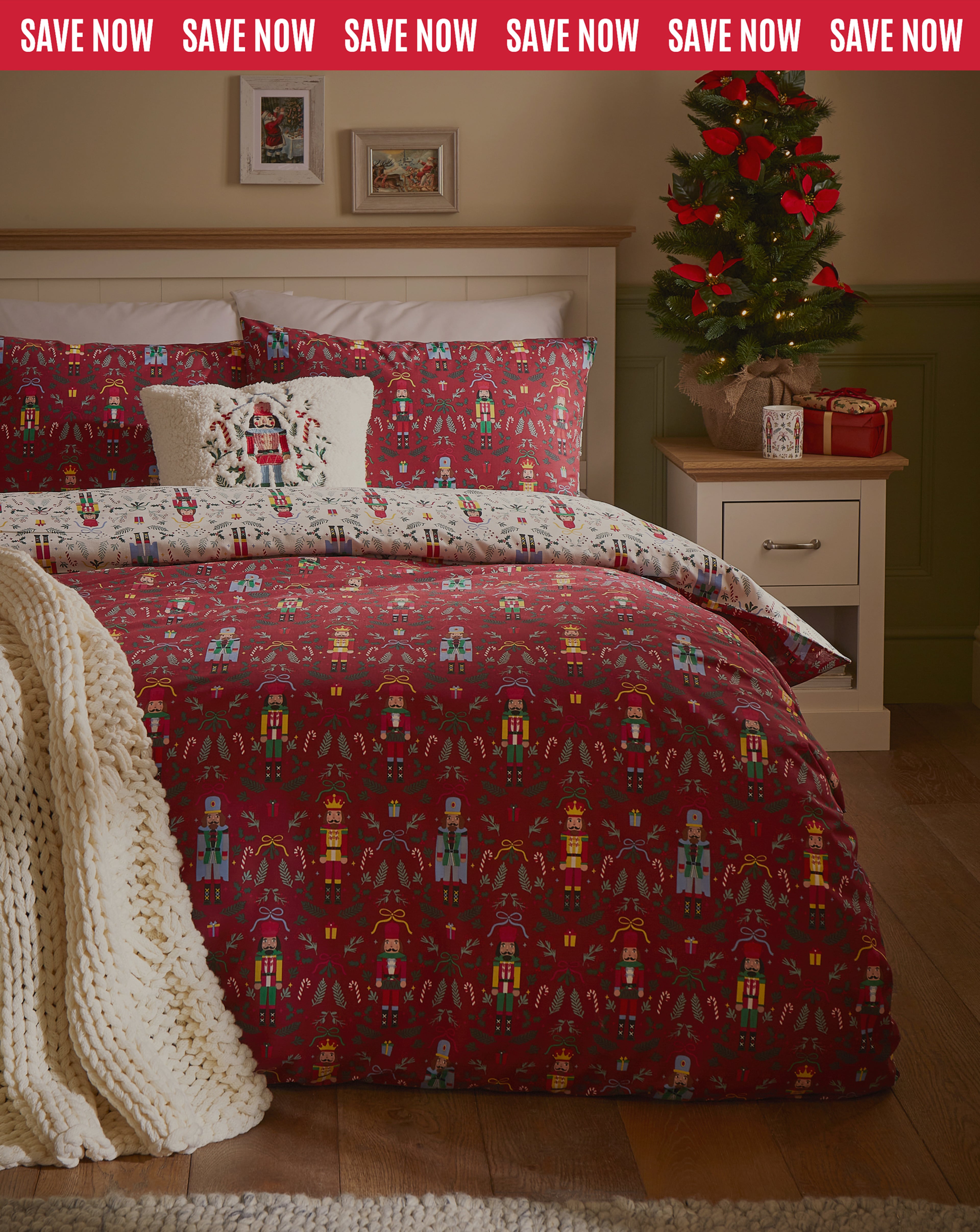 Festive bedroom with red nutcracker-themed bedding, white throw, and small Christmas tree on bedside table.