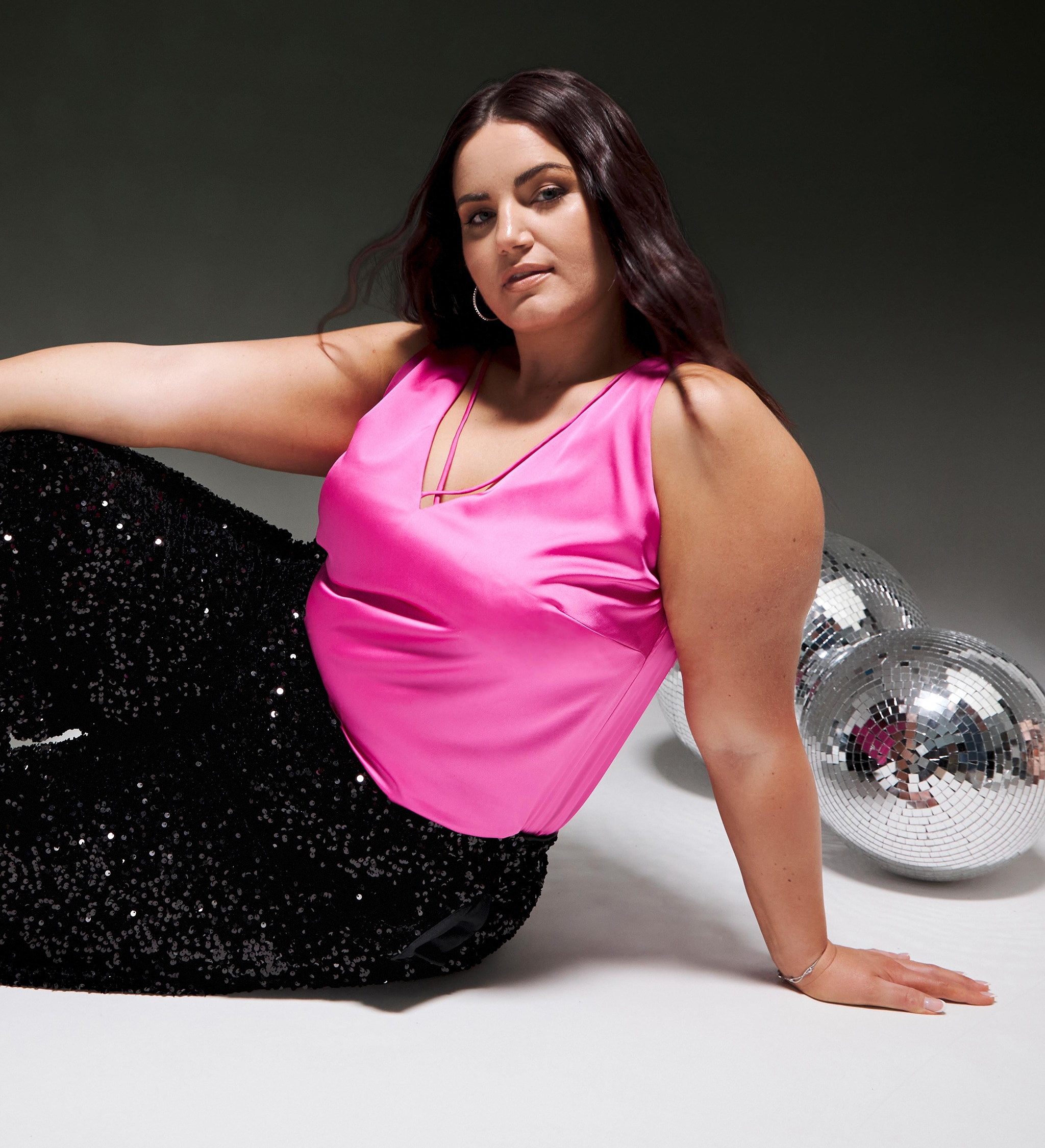 A woman sat wearing a sparkly pink vest top and sparkly black trousers