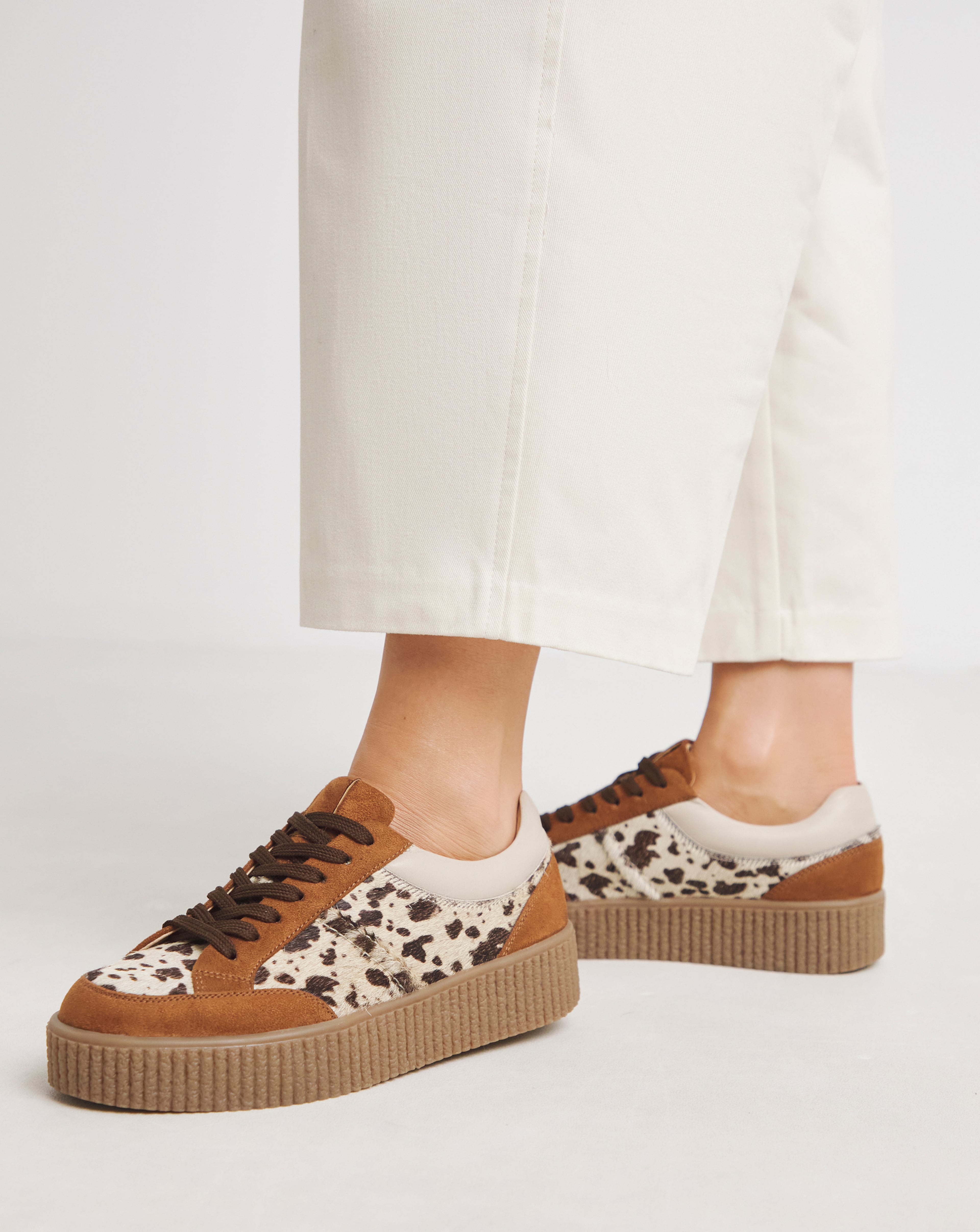 Close-up of a person wearing cream trousers and platform trainers with an animal-print design.