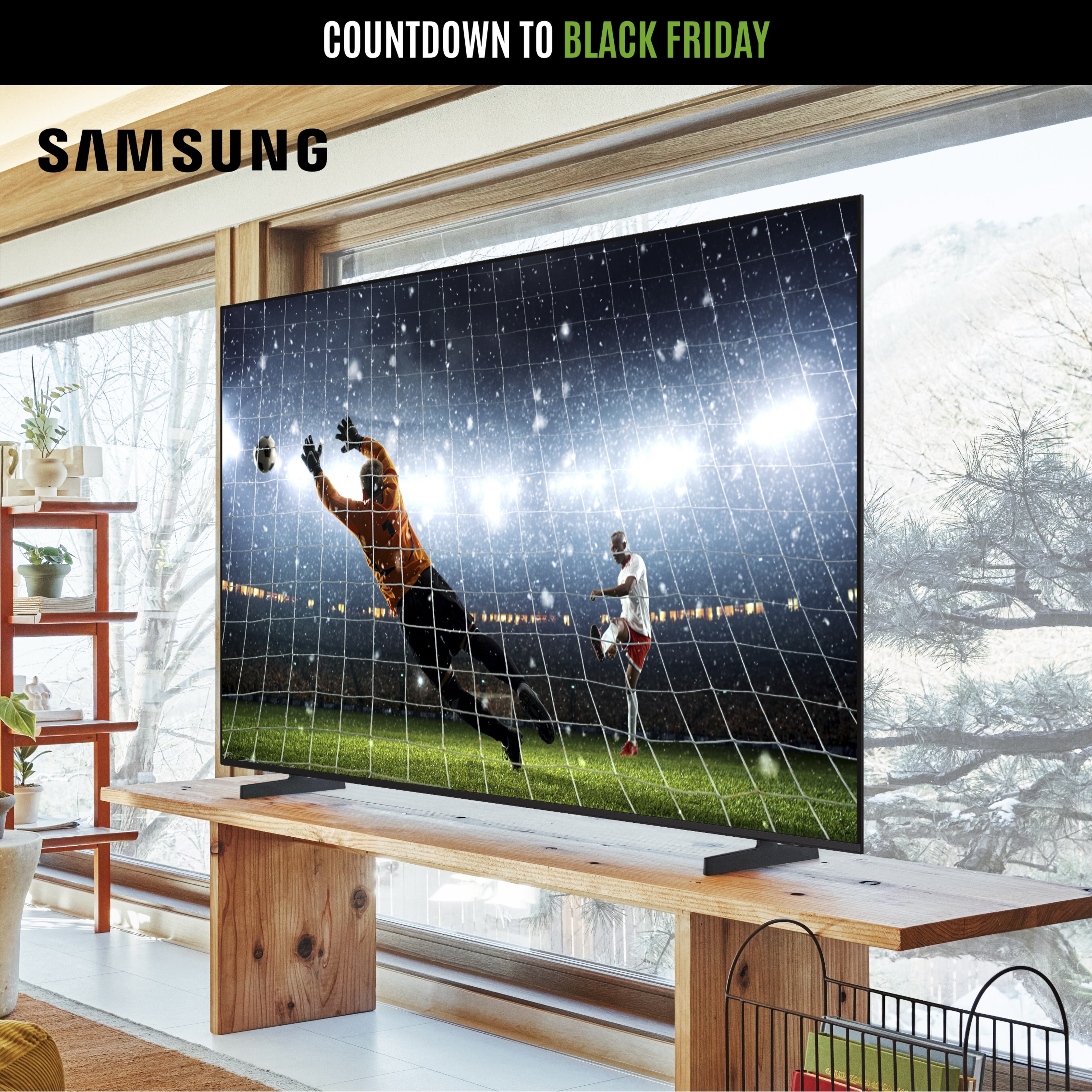 A Samsung TV on a wooden stand showing a football match, in a bright living room.