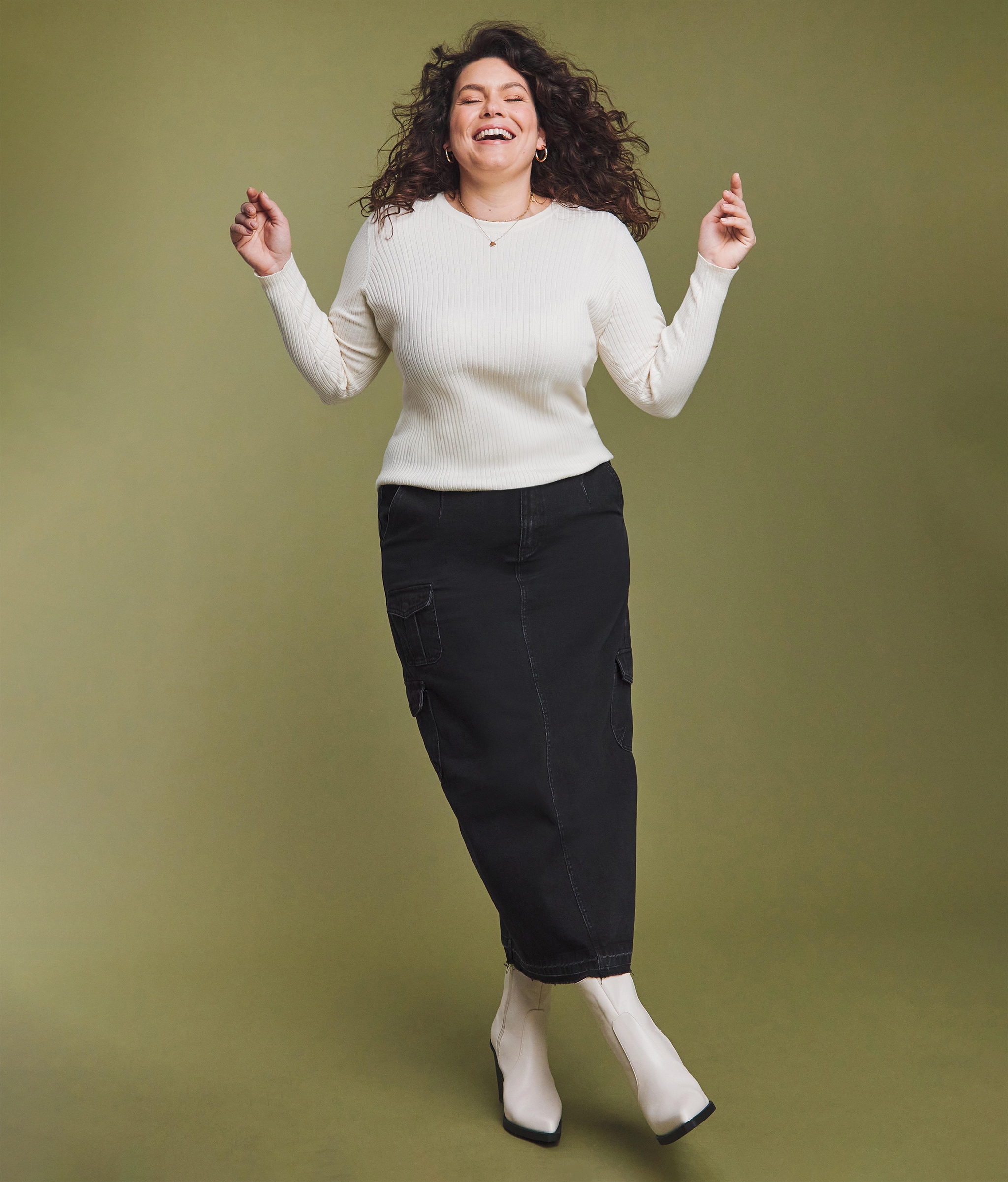A woman stood wearing a white jumper and long black skirt with white boots