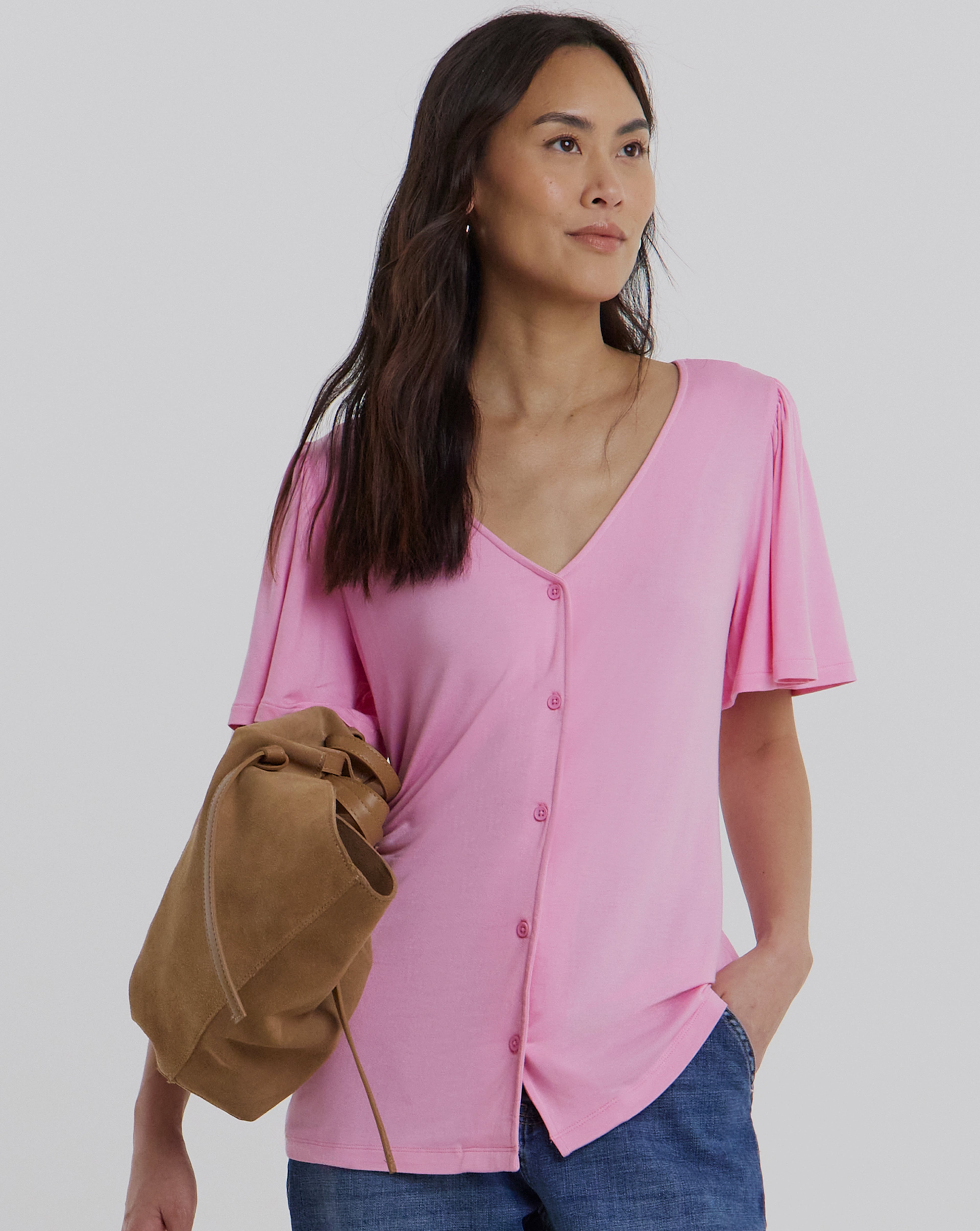 A model wearing a pink button front angel sleeve top and blue jeans.