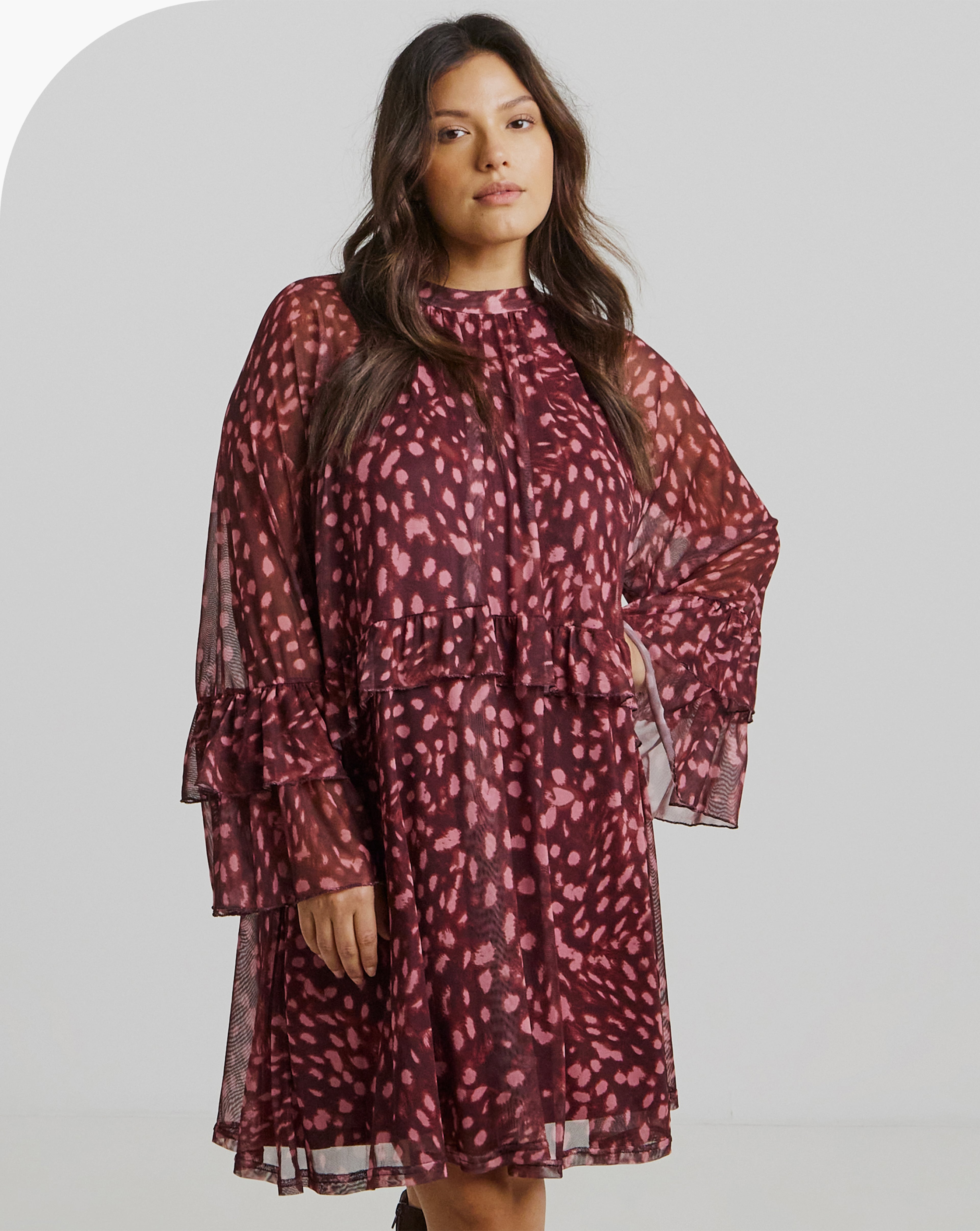 A person is wearing a loose-fitting, long-sleeve dress. The dress is sheer with a maroon base and pink abstract spots.